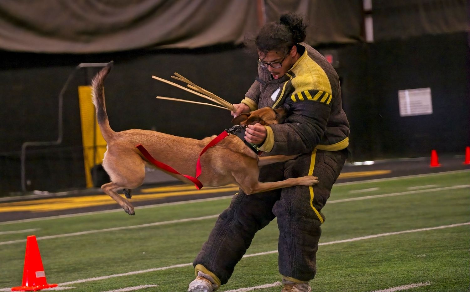 Two martial artists practicing stick fighting techniques during a training session on an indoor sports field.