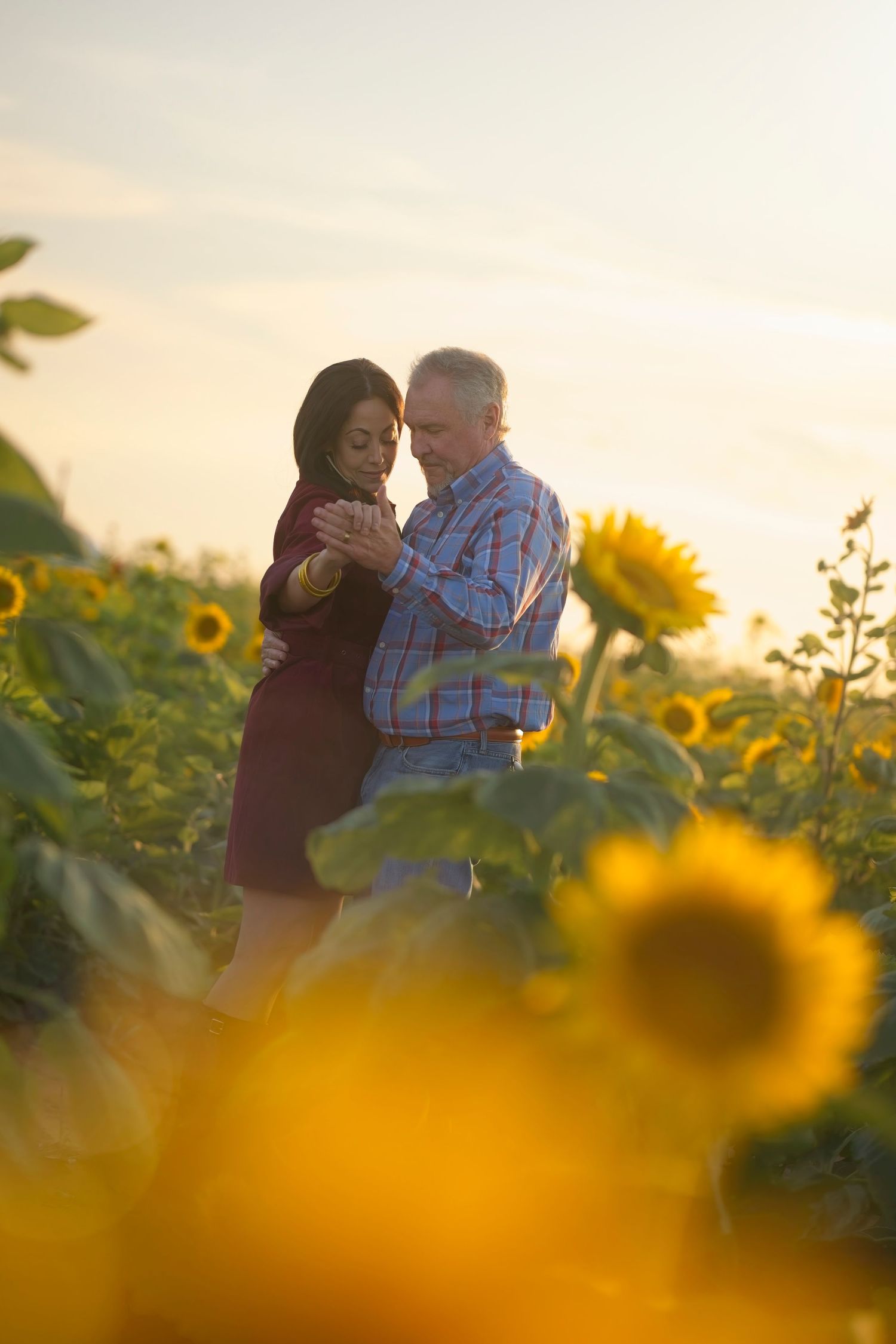A couple embraces in a sunflower field at sunset with golden light filtering through the blooming flowers.