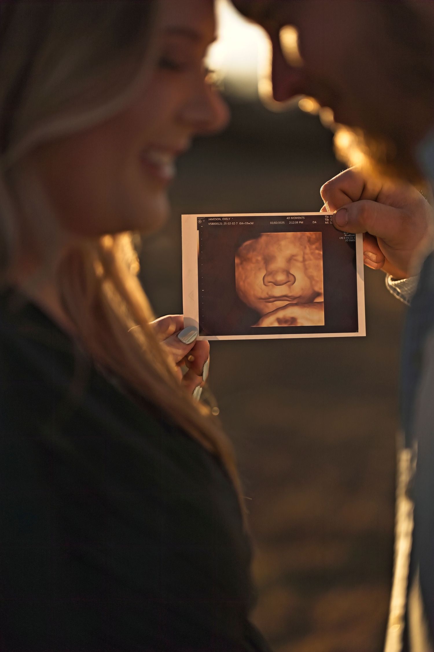 Someone holds up an ultrasound photo showing a baby against a dark background with warm lighting.