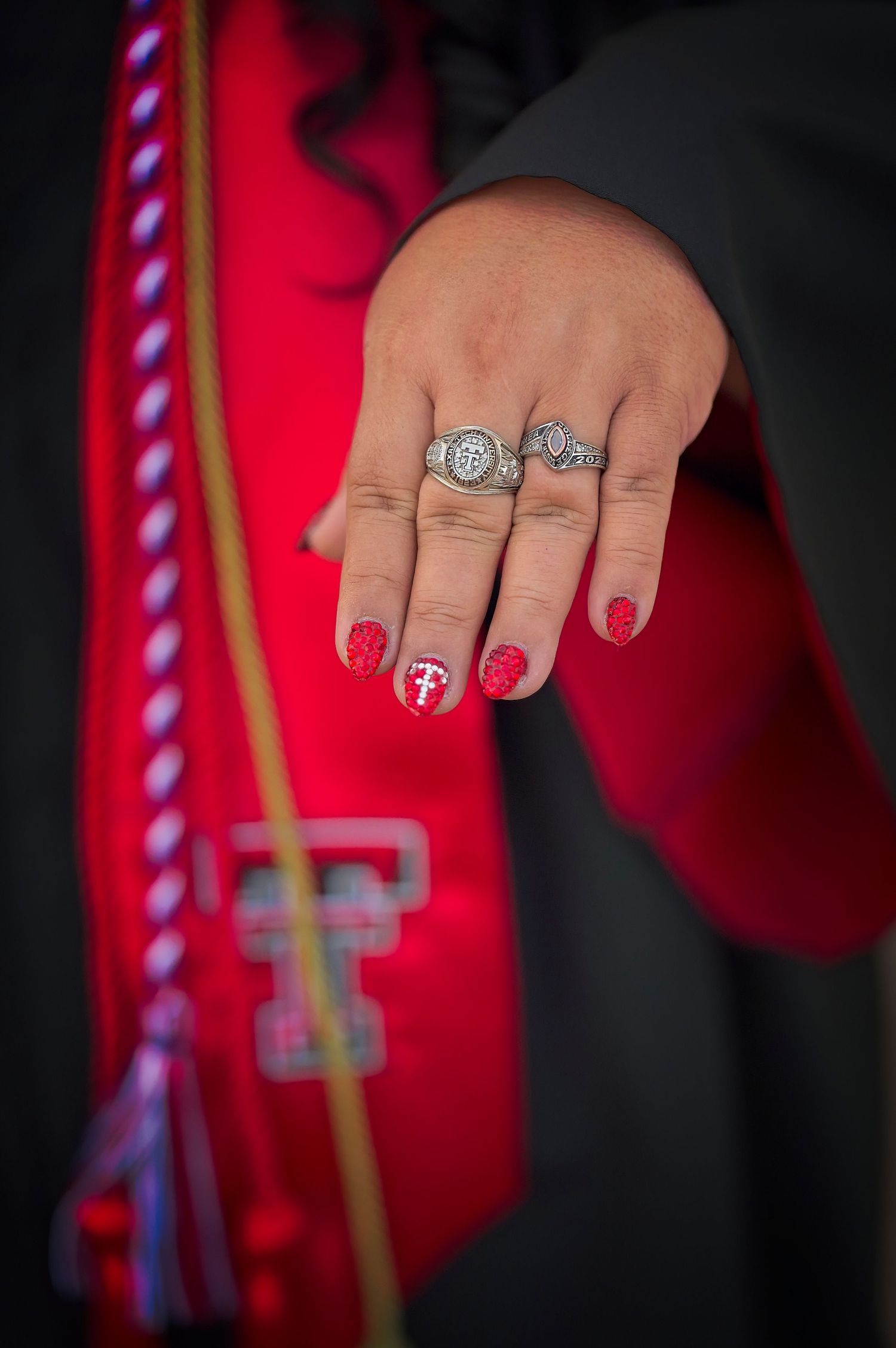 Close-up of decorated graduation ring and painted nails against red graduation gown.