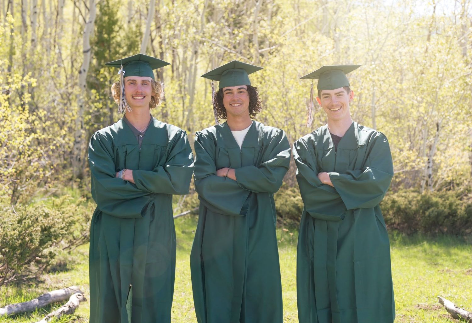 Group of graduates in emerald green robes posing together outside on a sunny spring day.