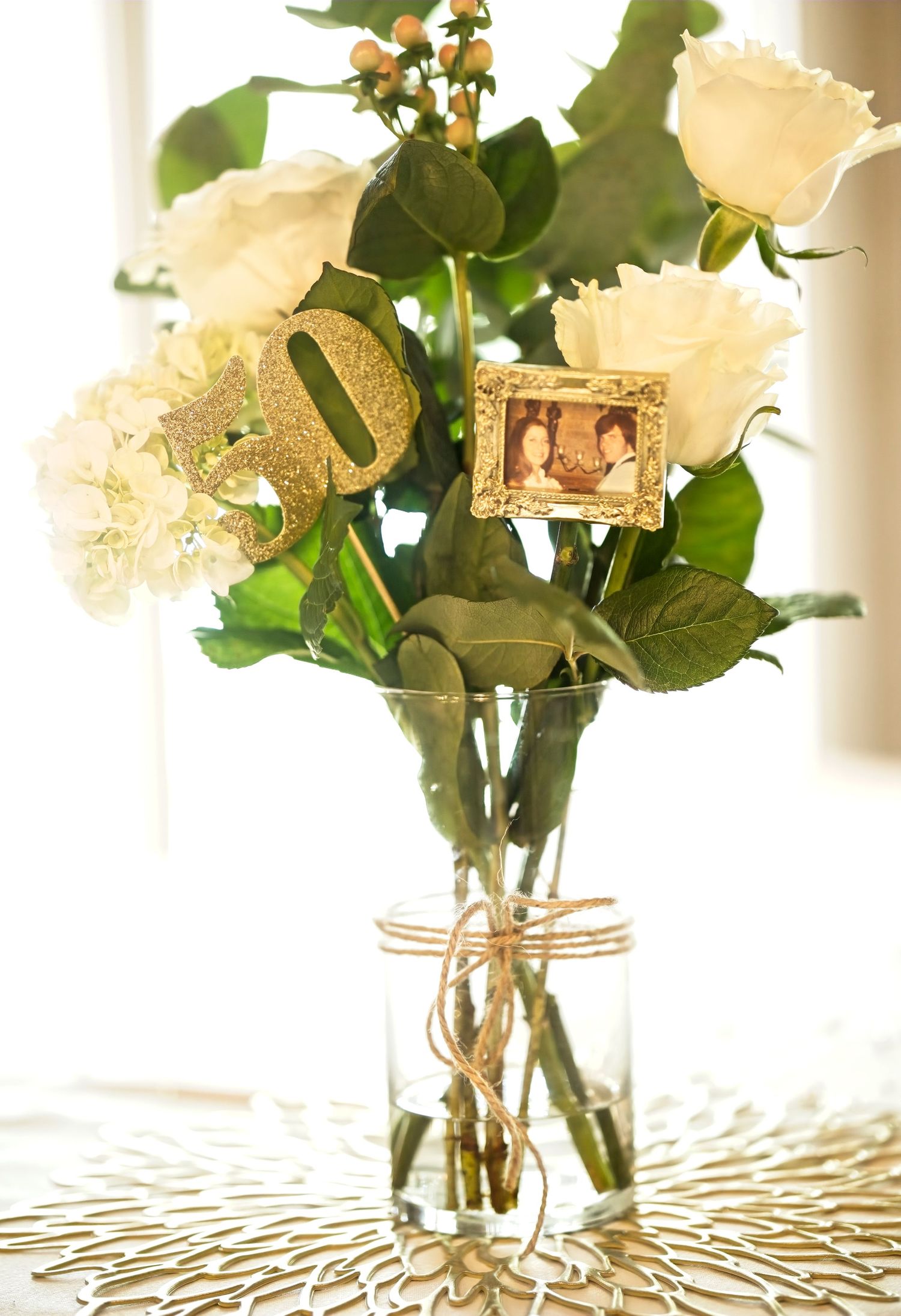 White roses in clear glass vases arranged on a table with natural window lighting.