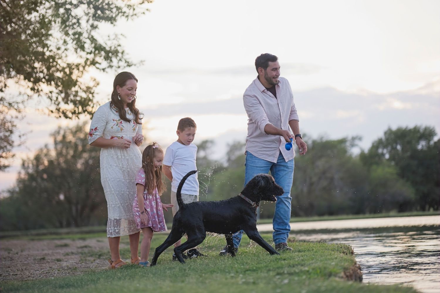 Family enjoying an evening walk with their dog near a lake at sunset.