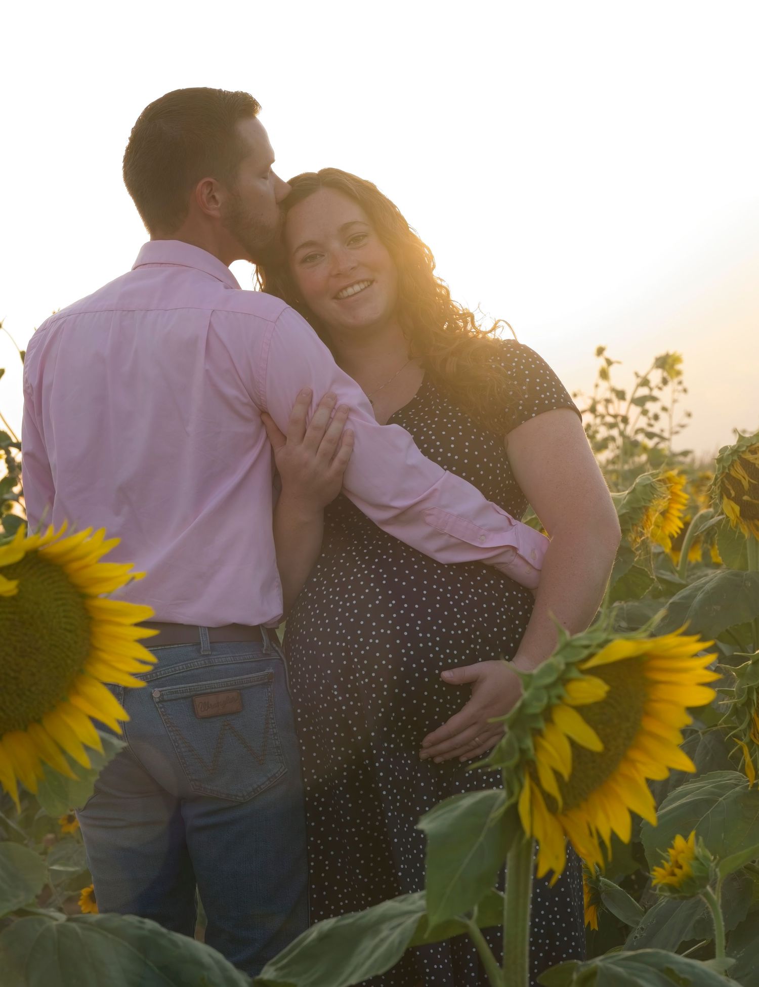 Romantic couple embraces in a sunflower field at sunset with golden sunlight illuminating the scene.