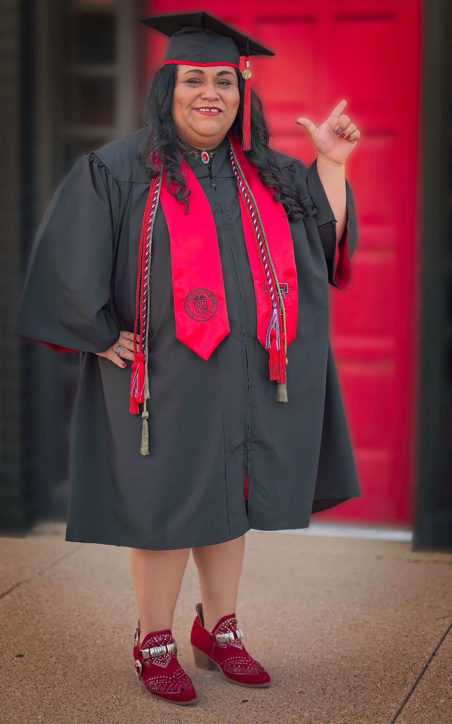 Graduate in cap and gown with red stole posing against red background.
