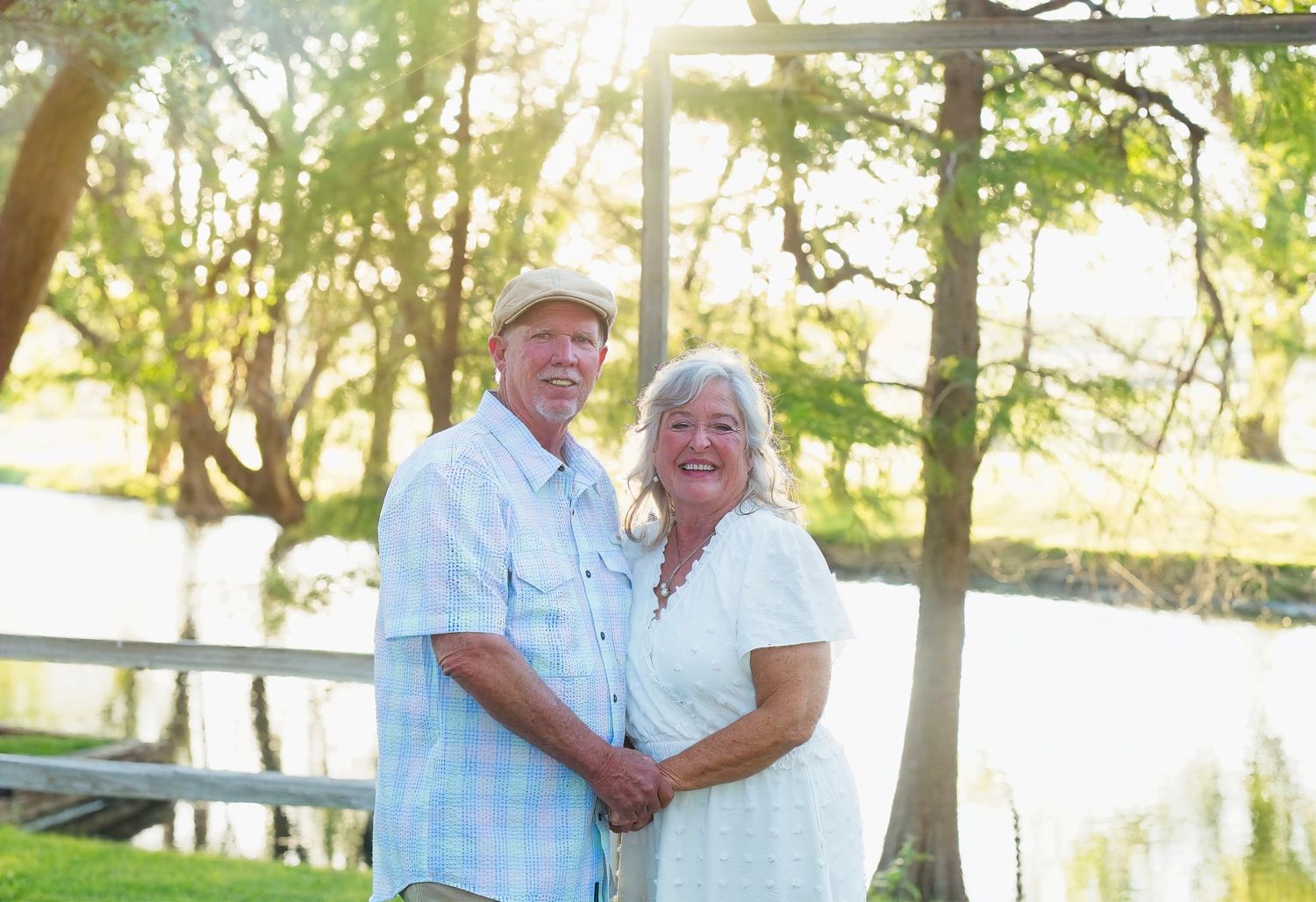 Couple in light summer clothing standing together by a serene lake on a sunny day.