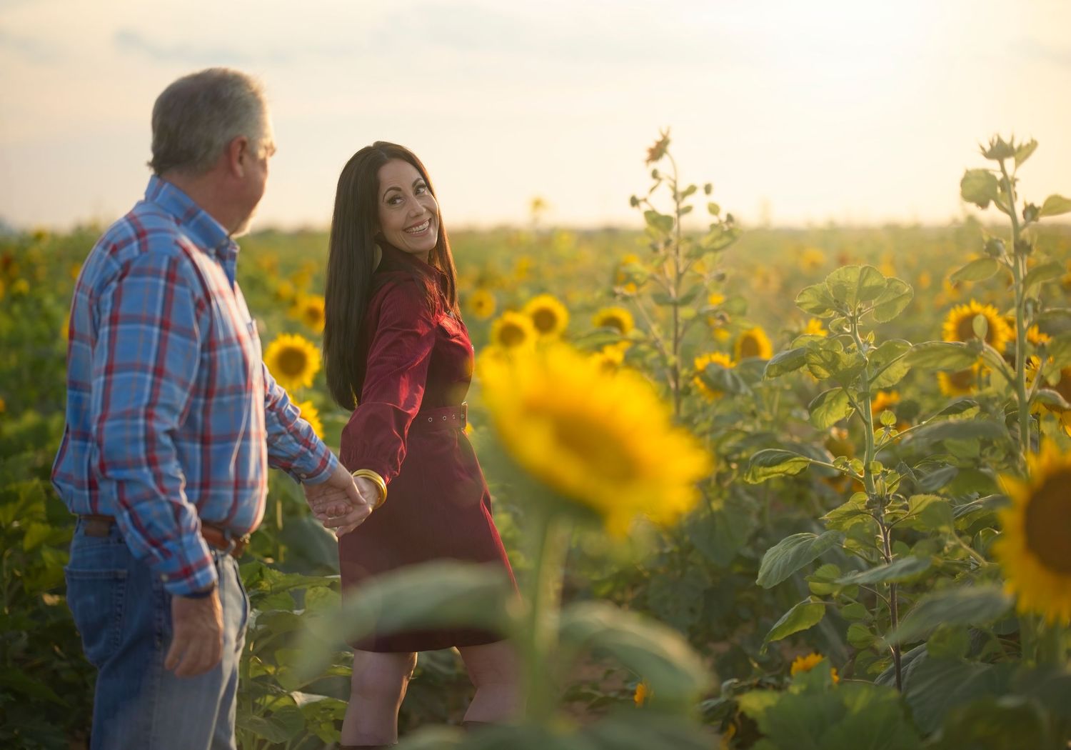 Two people share a romantic moment together in a golden sunflower field at sunset.