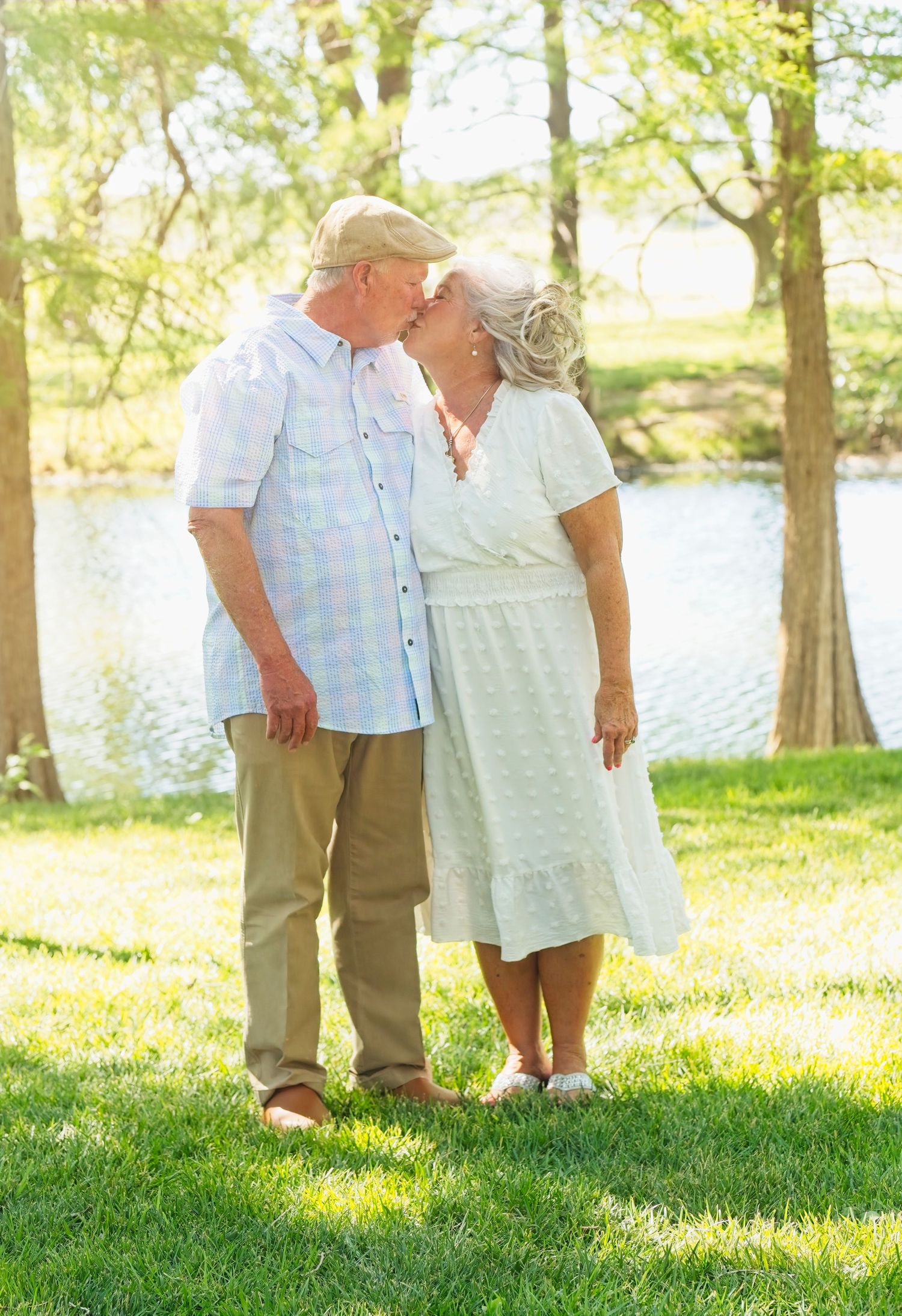 Outdoor family photo session with people standing on grass near a lake.