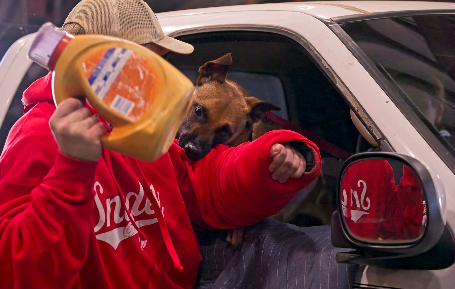 A hand holds an orange beverage cup with a straw through a car window at a drive-thru restaurant.