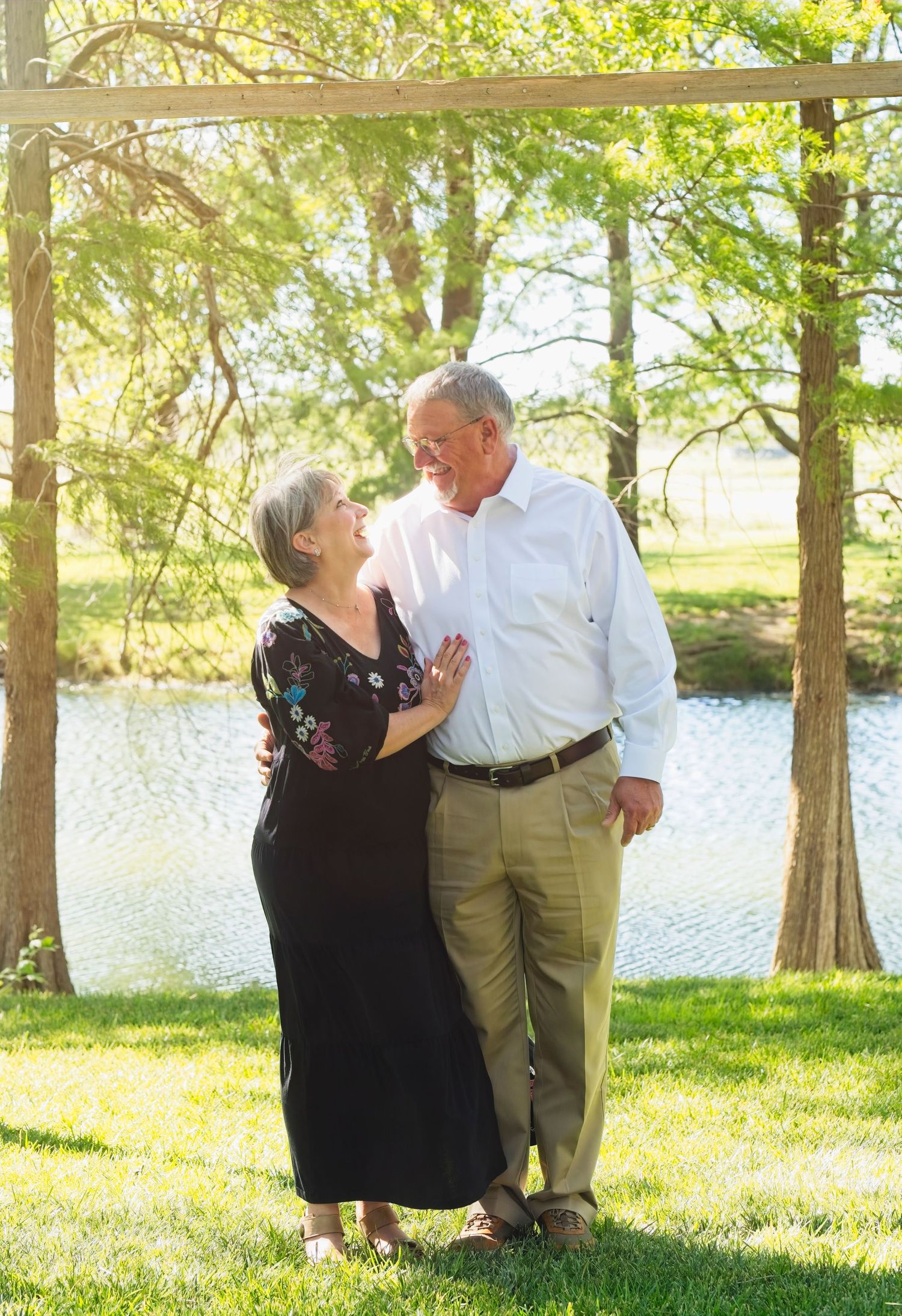 A couple shares a tender moment together by a tranquil lake on a sunny afternoon surrounded by cypress trees.