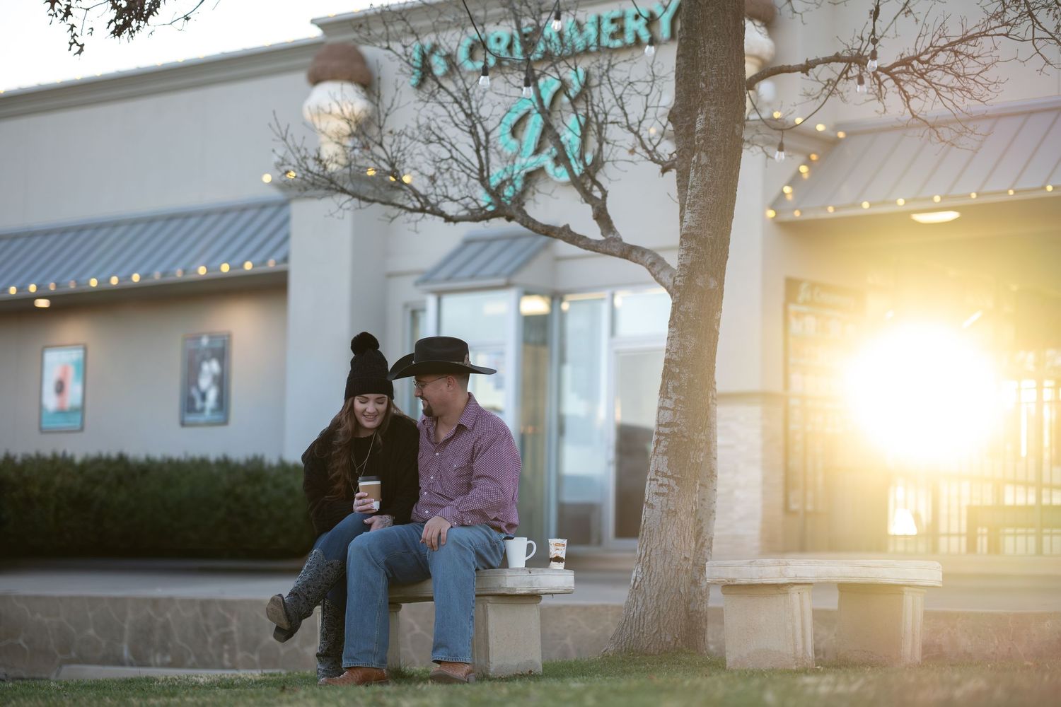Two people sit together on a bench in front of a house during a golden sunset.