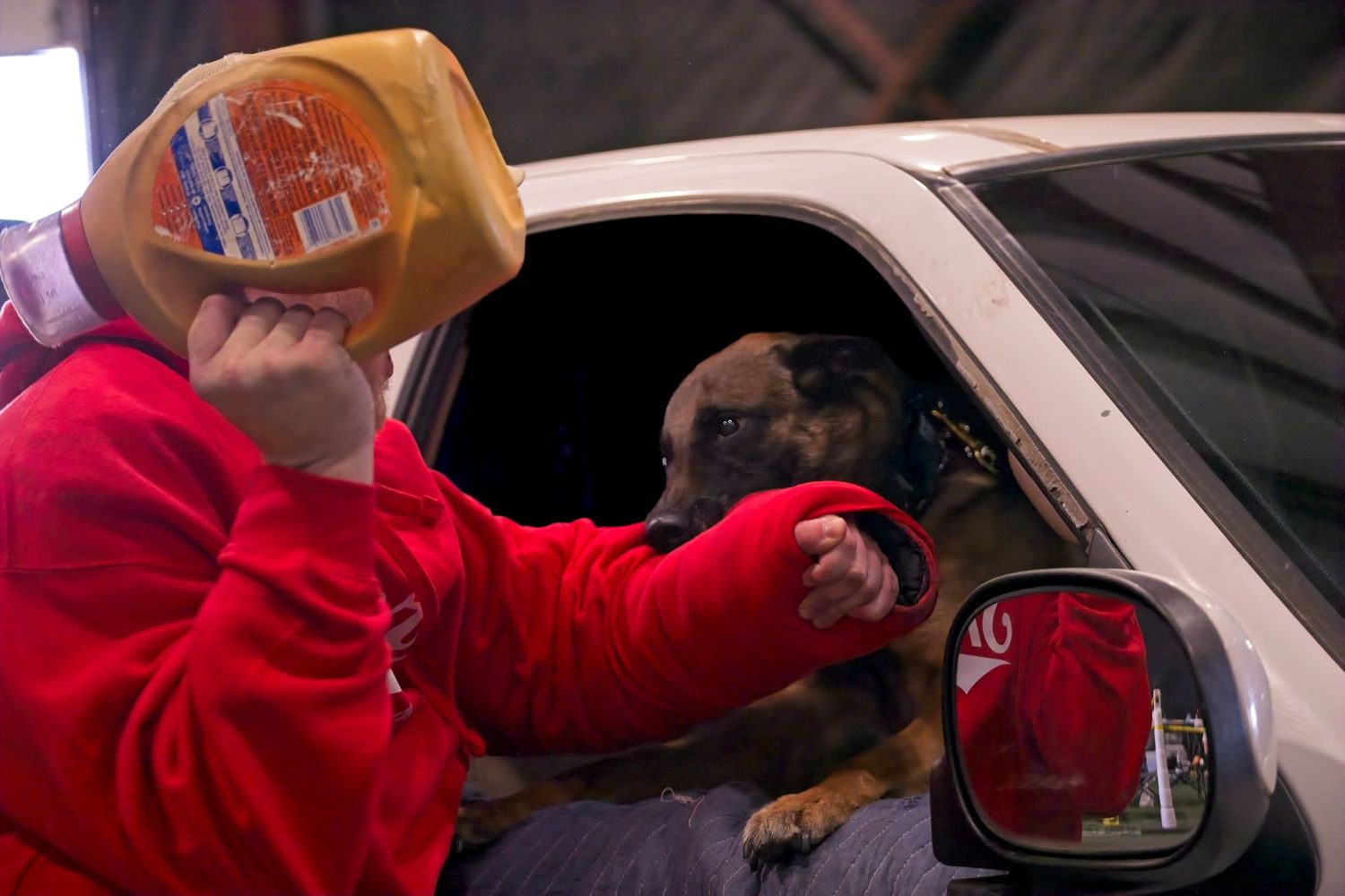 A person in a red jacket reaches through a car window to hand something to someone inside the vehicle.