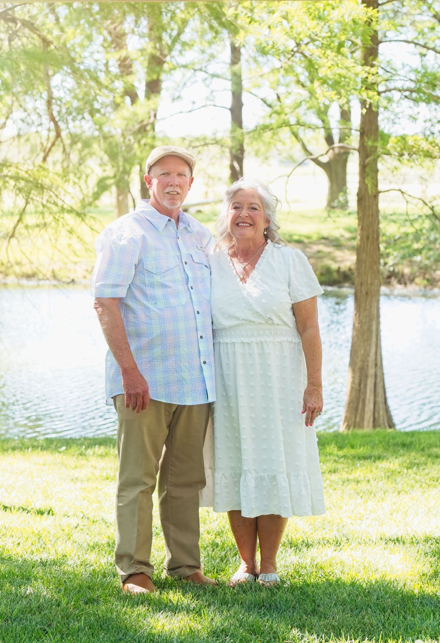 An elderly couple shares joyful moments by a serene lake surrounded by trees on a sunny afternoon.