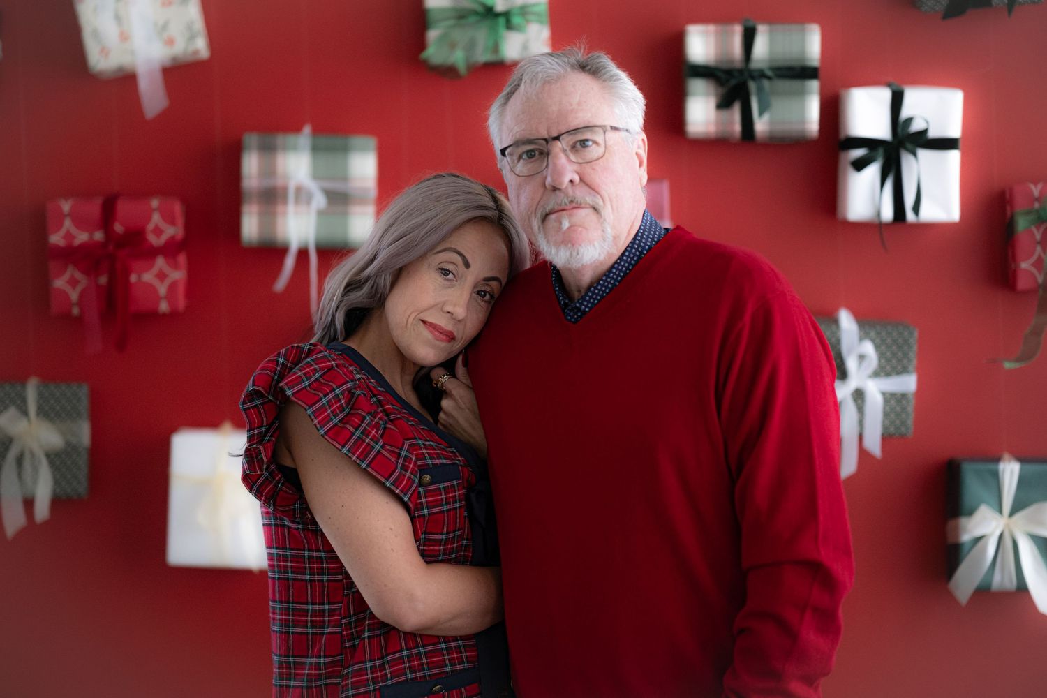 A couple embraces in a festive setting with red walls and silver decorative elements in the background.