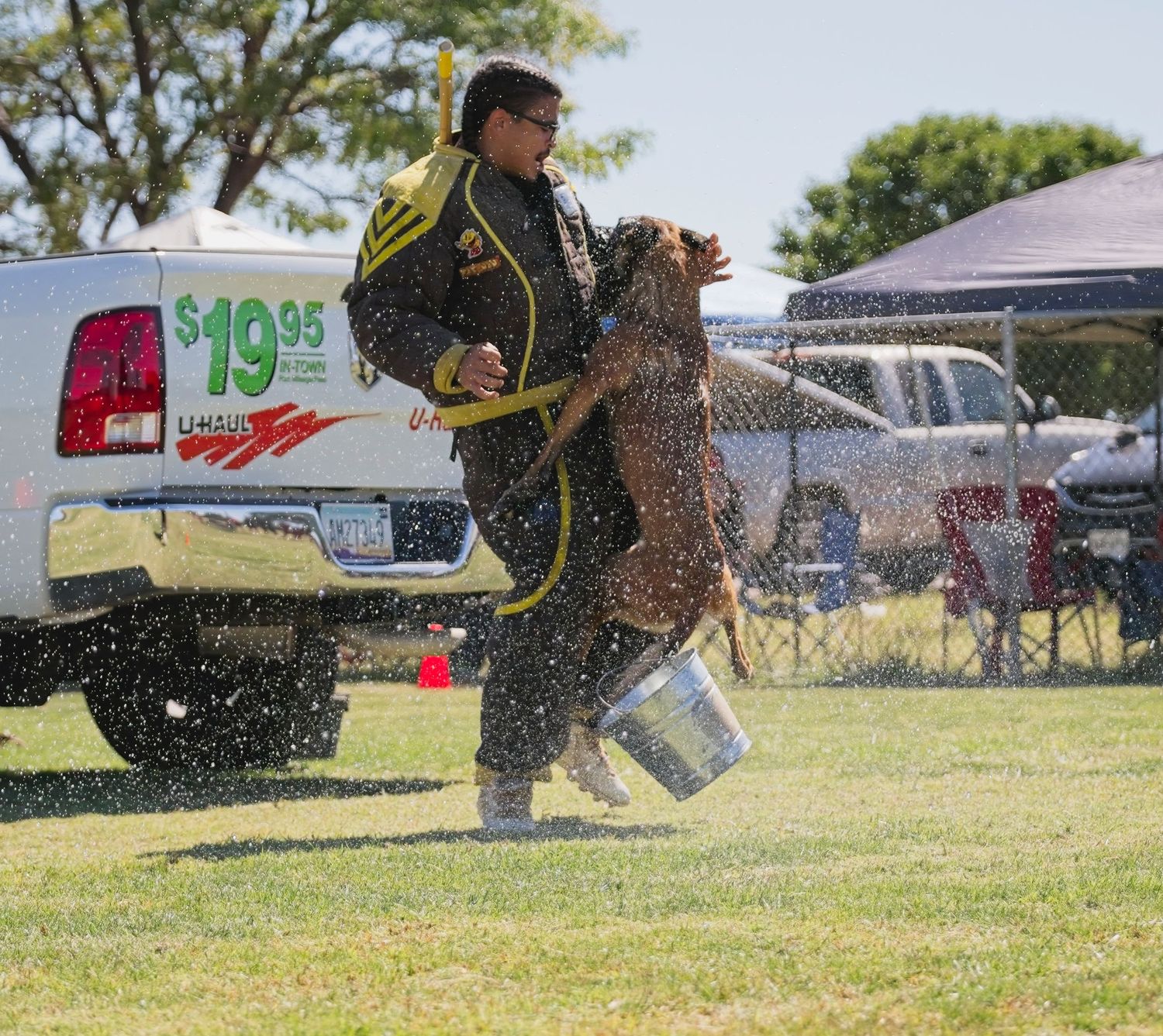 A sequence of action shots showing a police K9 dog leaping through water spray during outdoor training exercises.