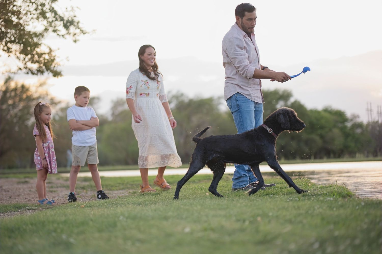 Family enjoying an evening walk with their dog near a lake at sunset.