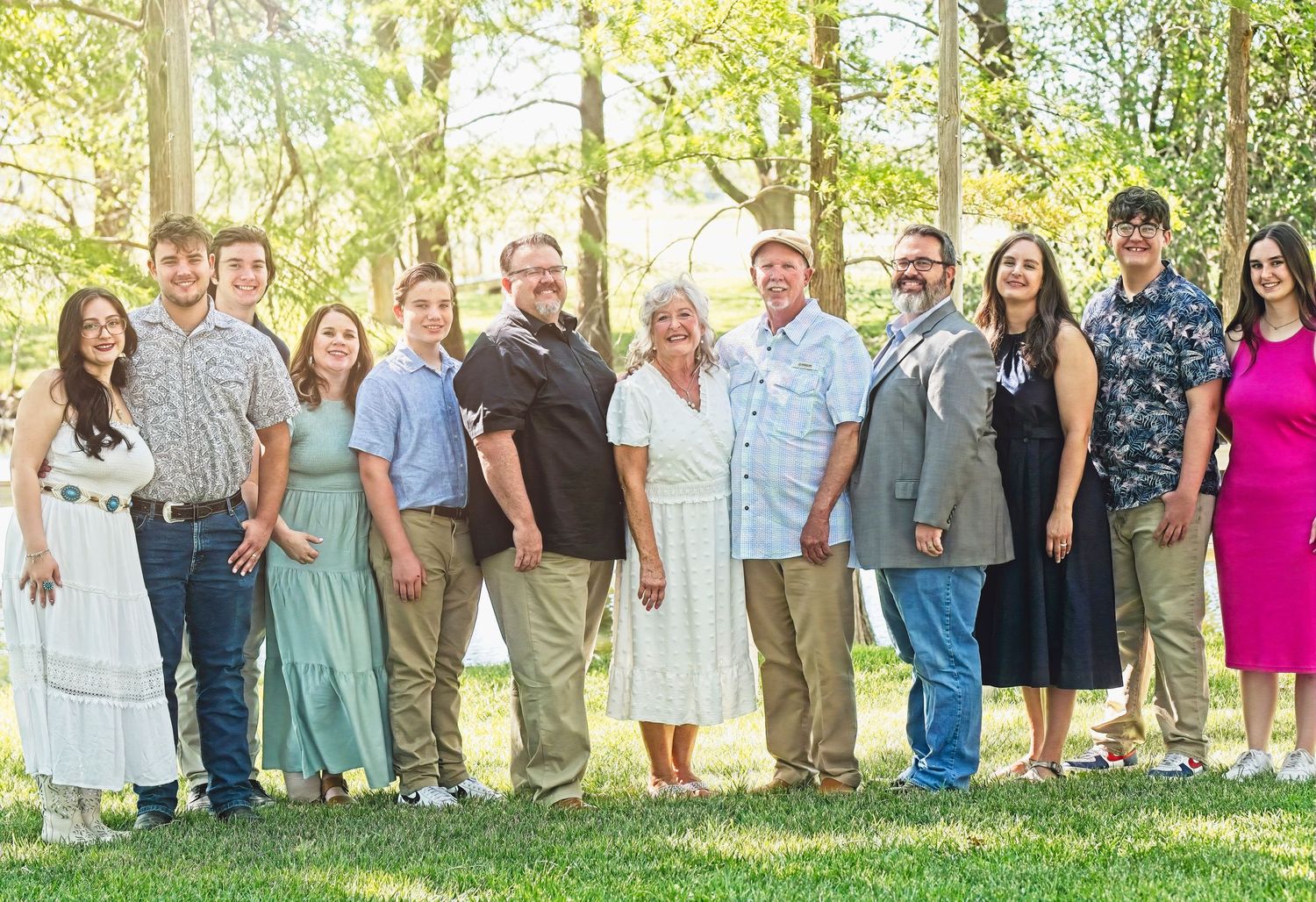 Large group portrait taken outdoors with everyone standing together on grass under trees.