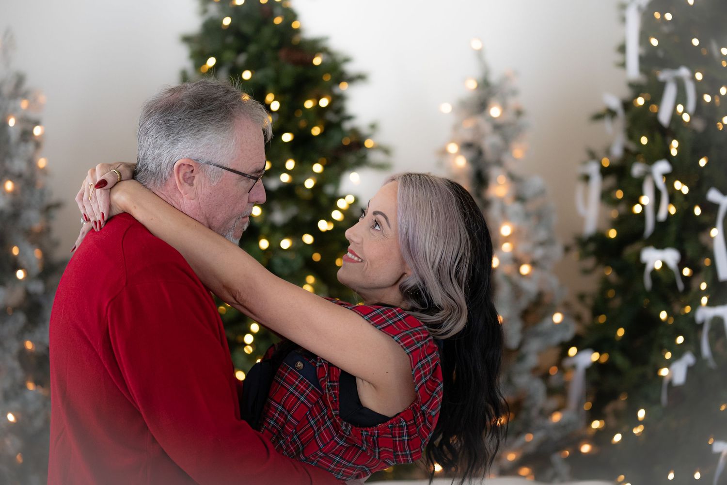 A couple shares a romantic moment in front of a decorated Christmas tree with twinkling lights.