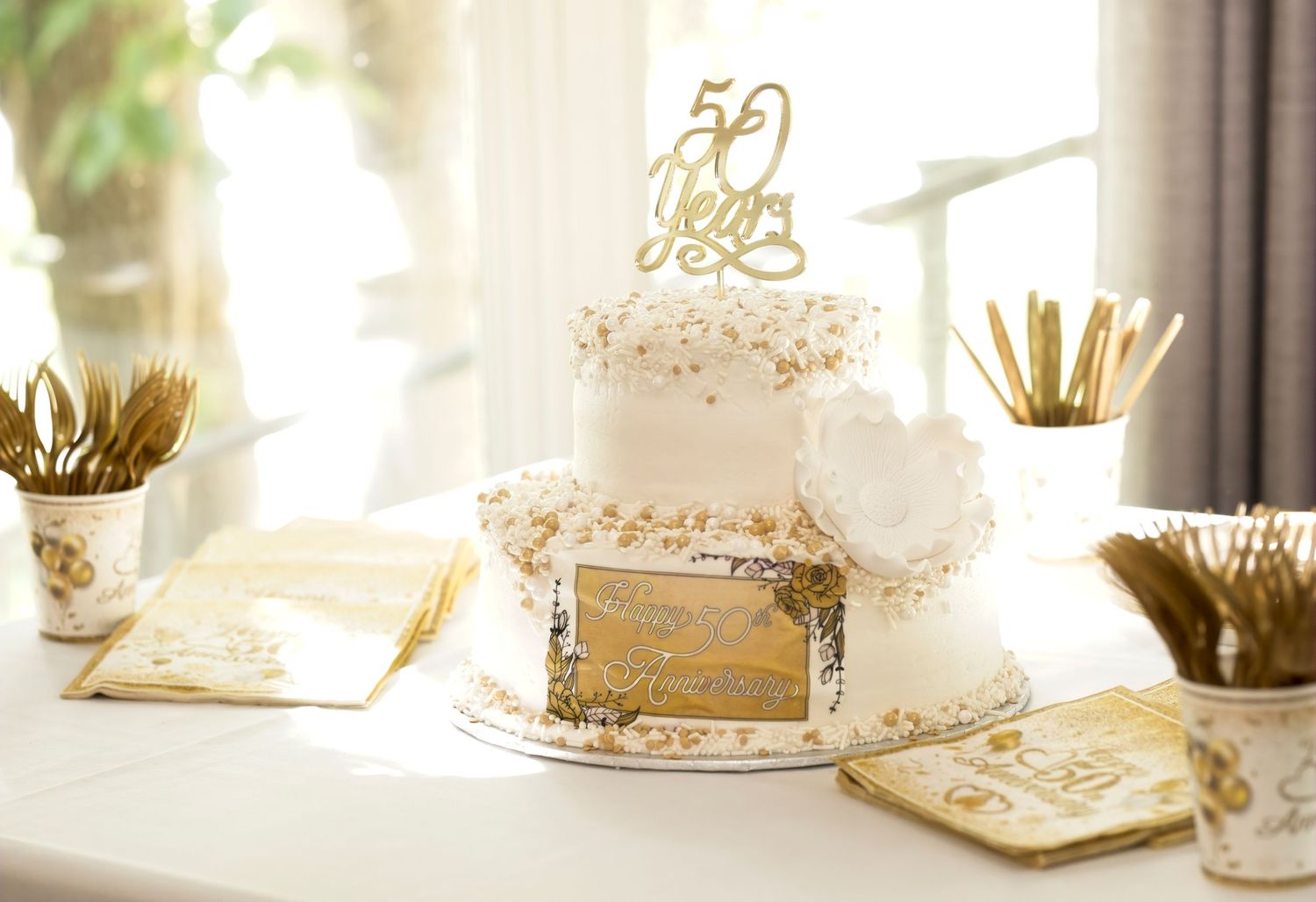 Elegant 50th anniversary celebration table setting with white and gold decorations.