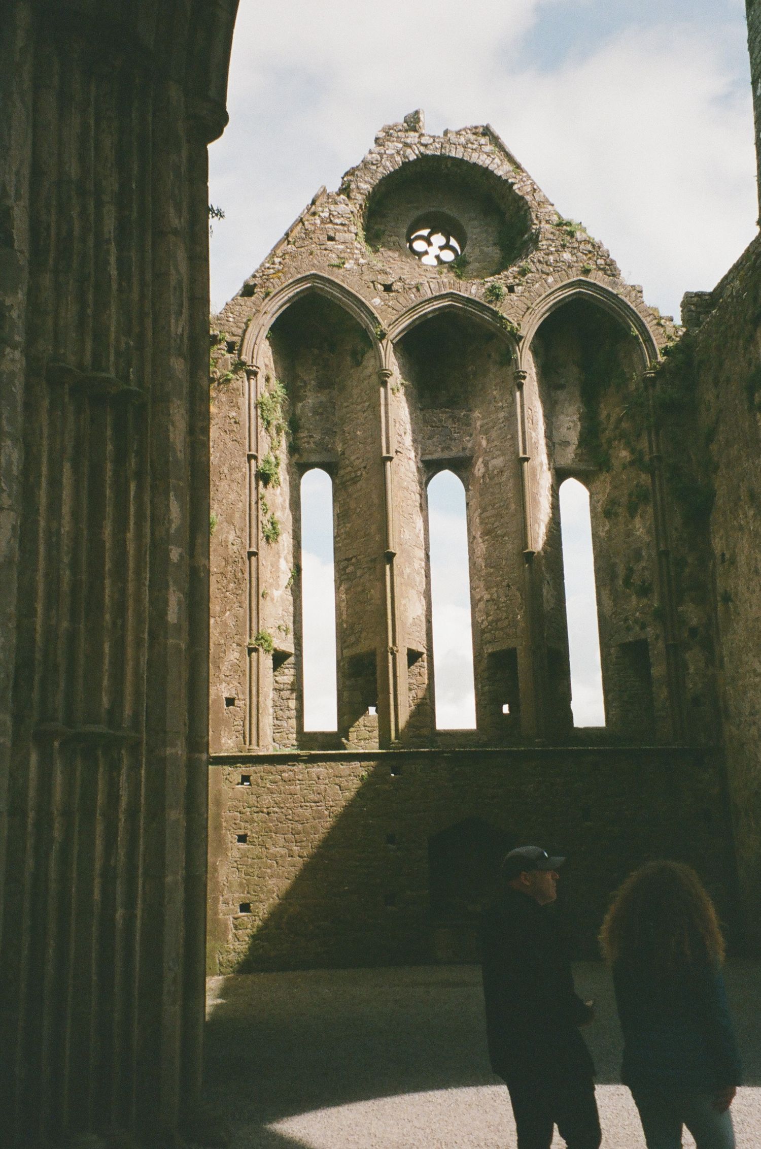 Ancient stone arches and tall windows line the interior of a historic Gothic cathedral ruin.