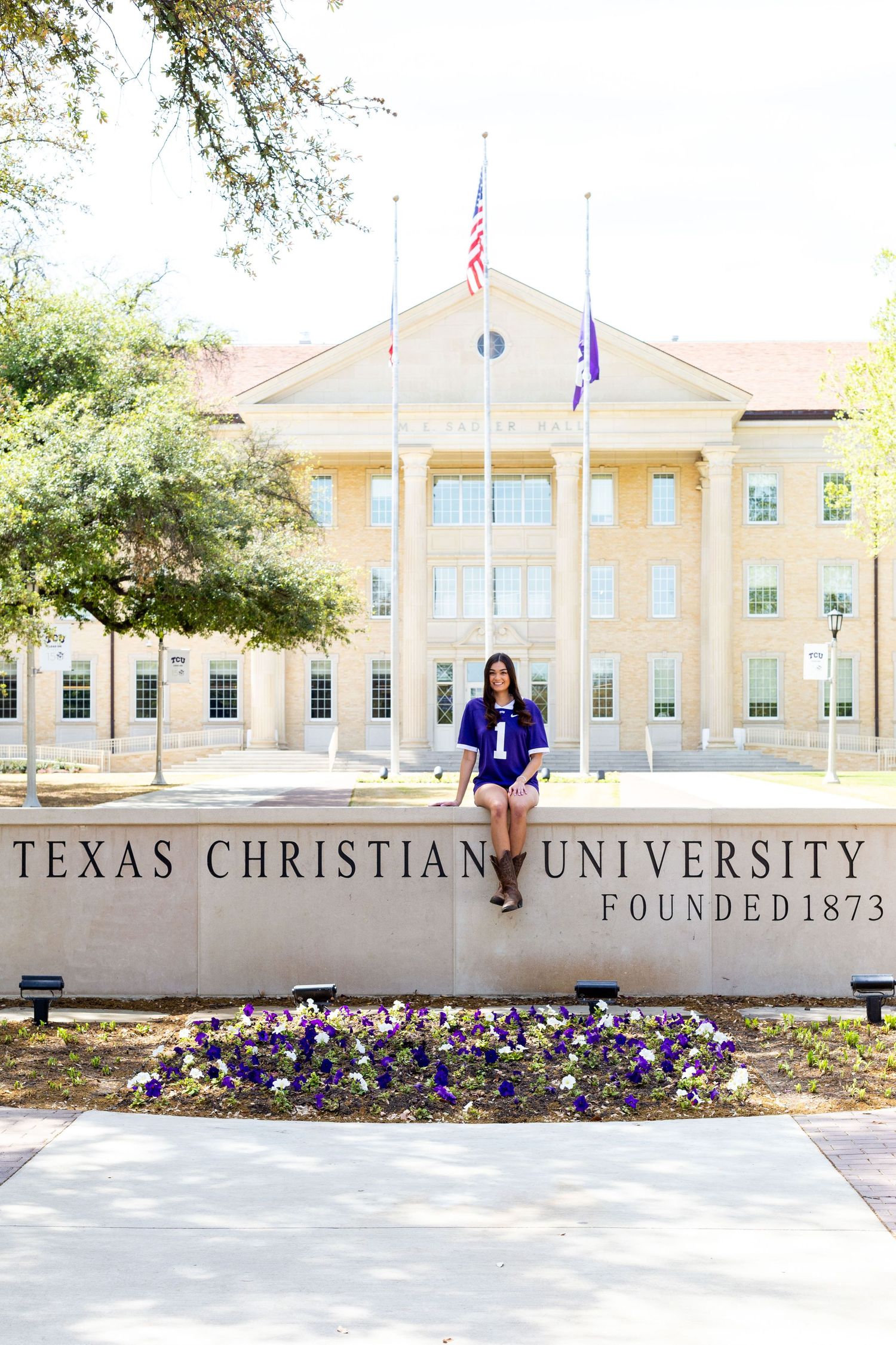 A collegiate building with columns and American flag at Texas Christian University with purple pansies in the foreground.