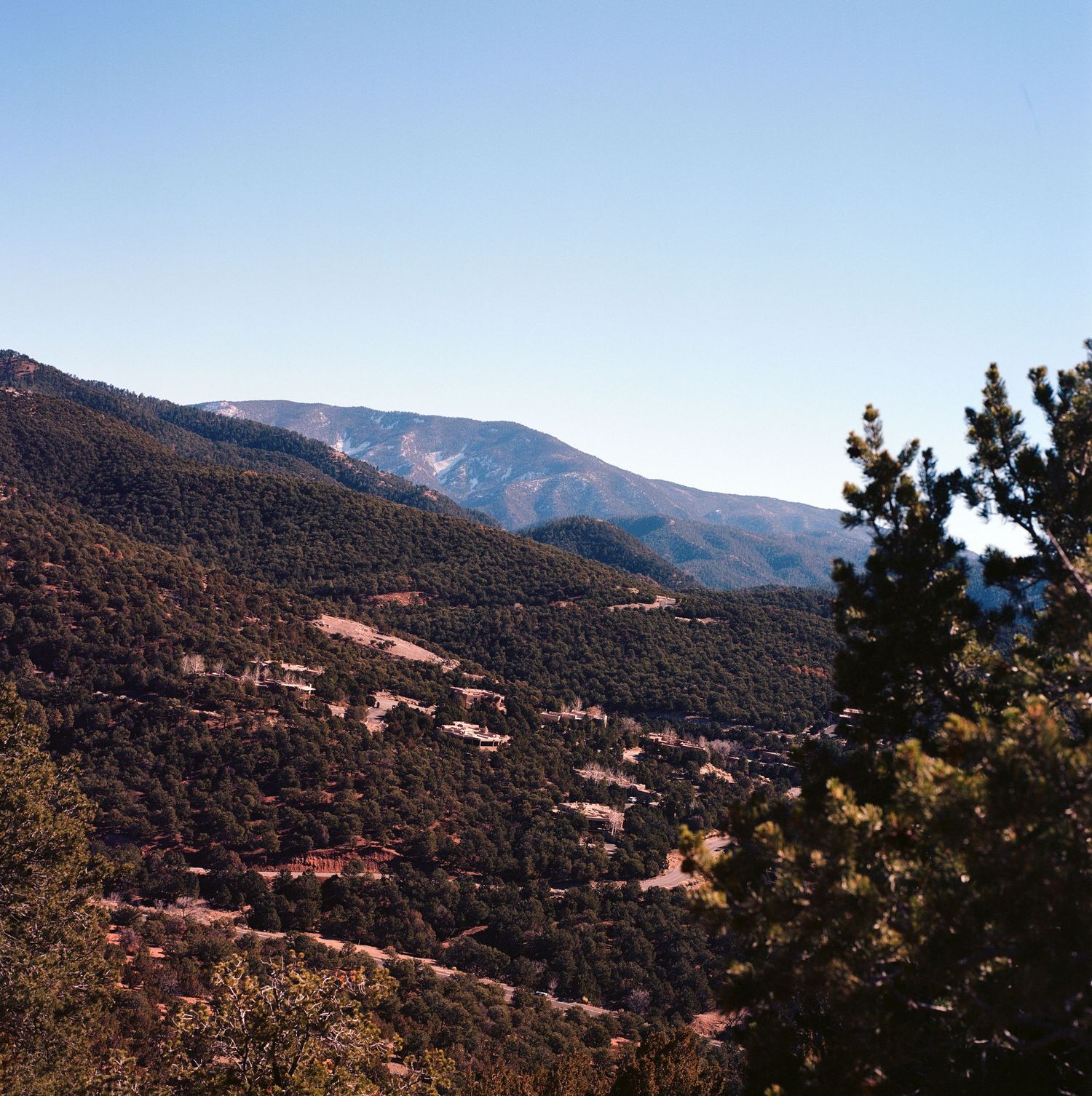 Mountain landscape view with forested slopes and rolling hills stretching into the distance under a clear blue sky.