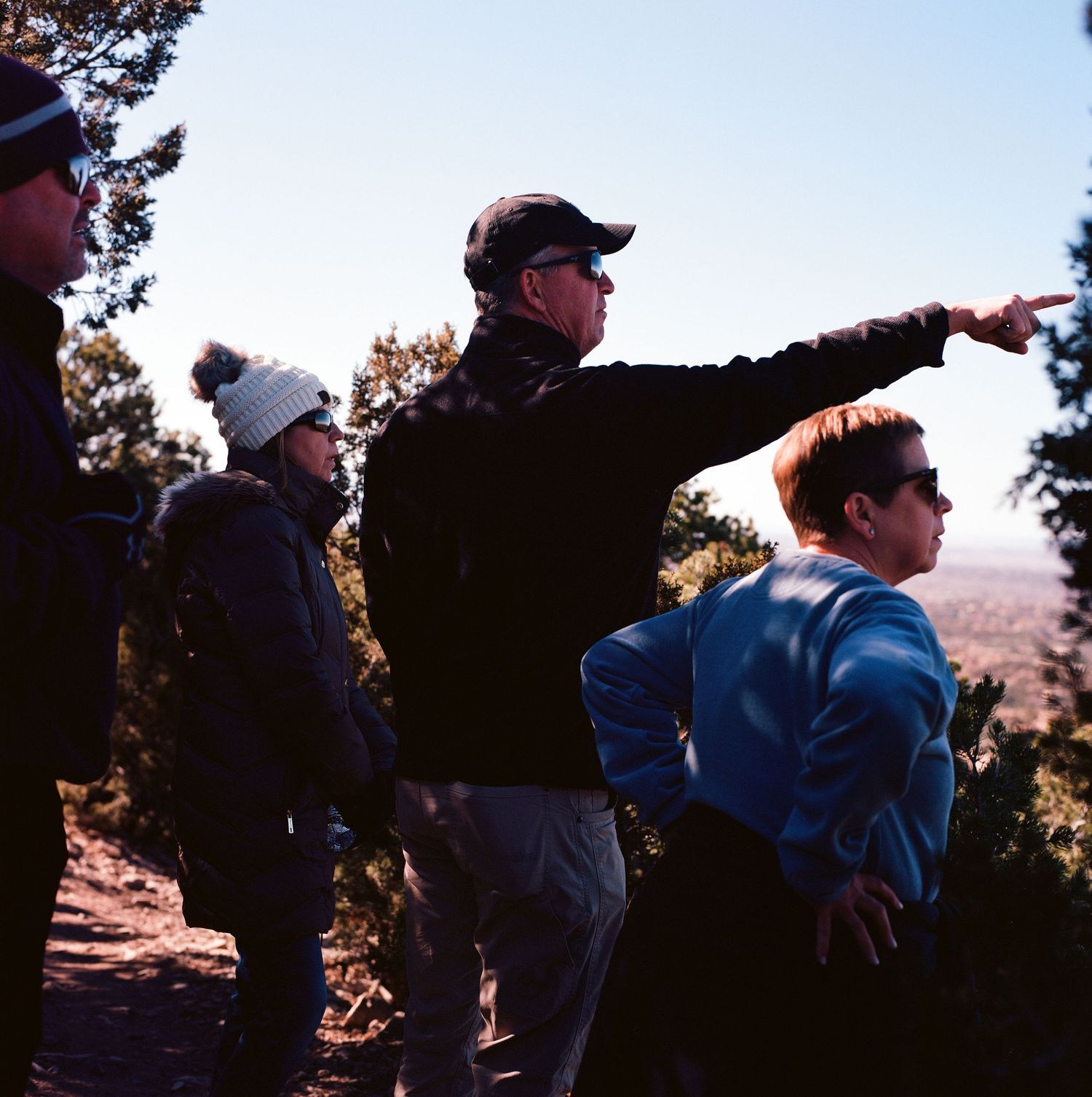 Outdoor group points and looks out at scenic mountain vista while standing near edge during daytime hike.