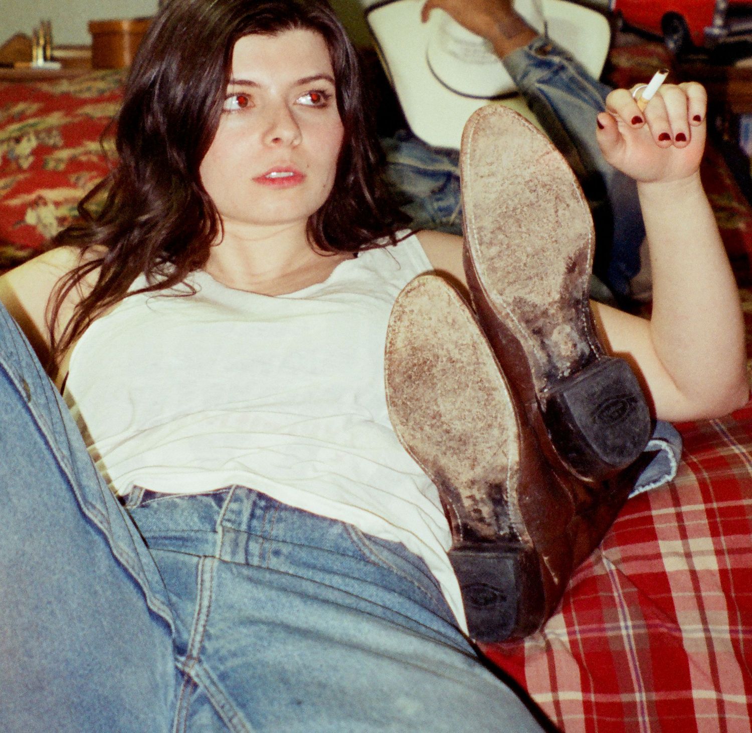 Person in casual attire lounging on plaid fabric with boots up, wearing white t-shirt and jeans in vintage style photo.