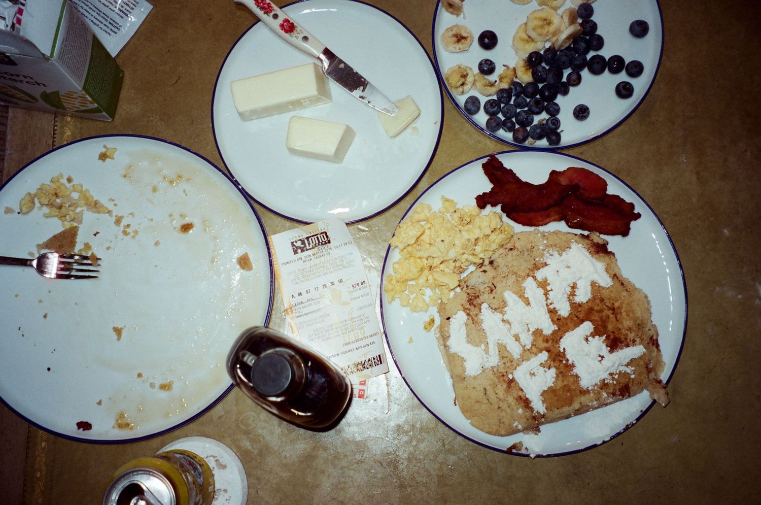 A messy dinner table with partially eaten plates of food, crumbs, cheese, and blueberries scattered on white dishes.