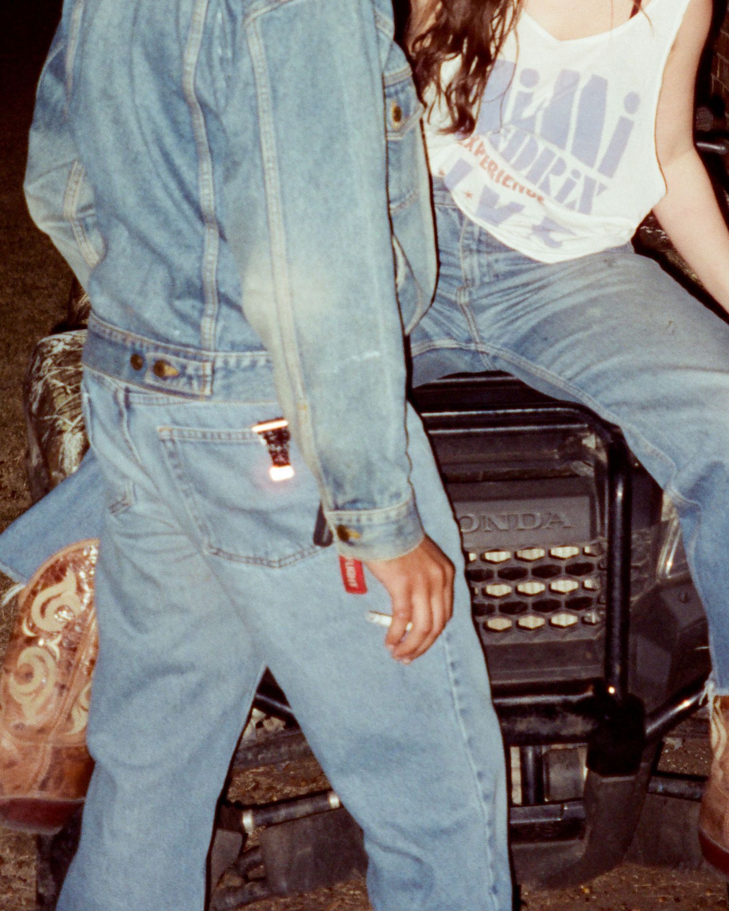 Casual retro fashion photo showing people in denim sitting together with a stone wall in the background.