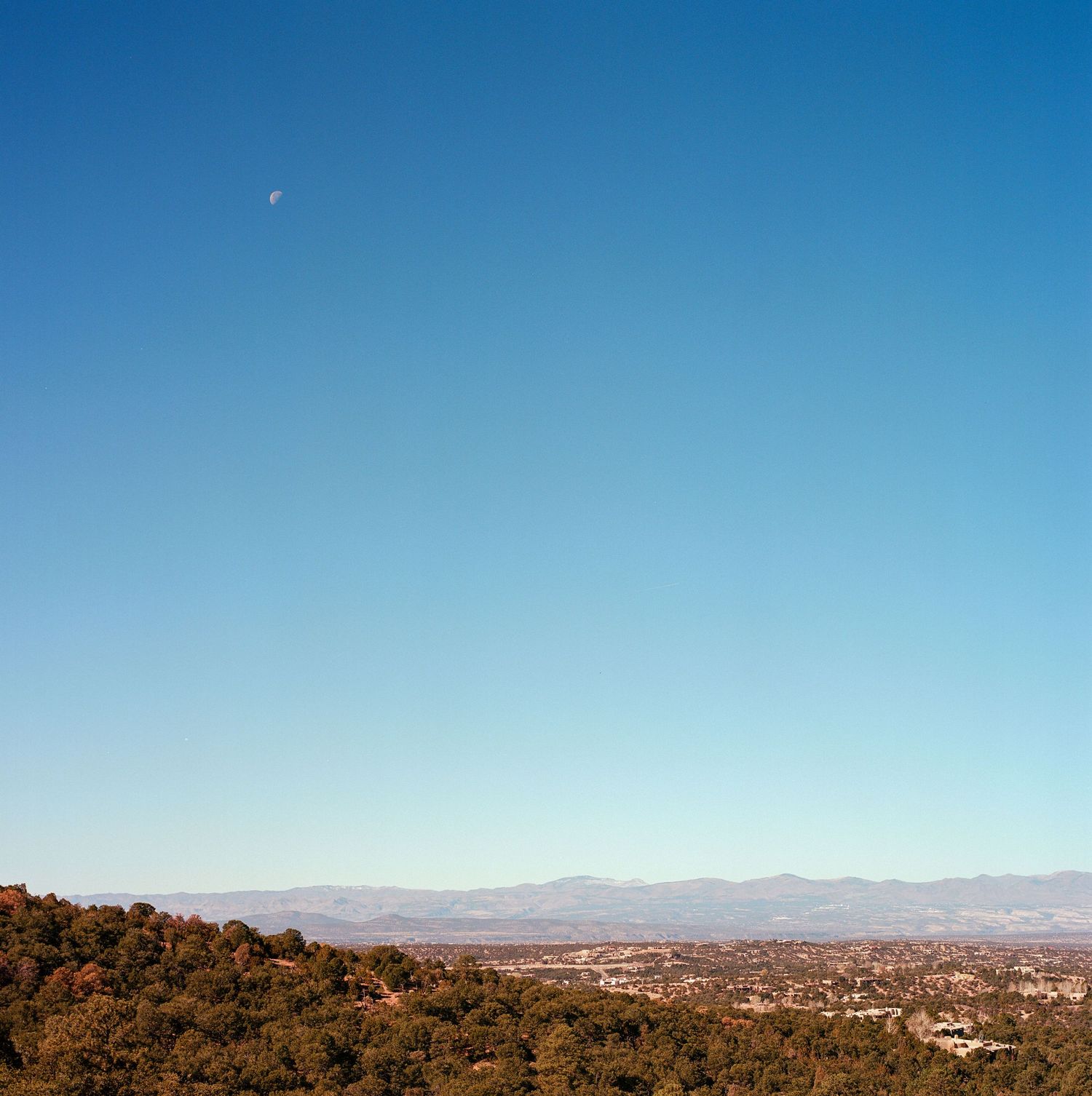 Aerial view of a hillside overlooking a desert valley with distant mountains under a bright blue sky.