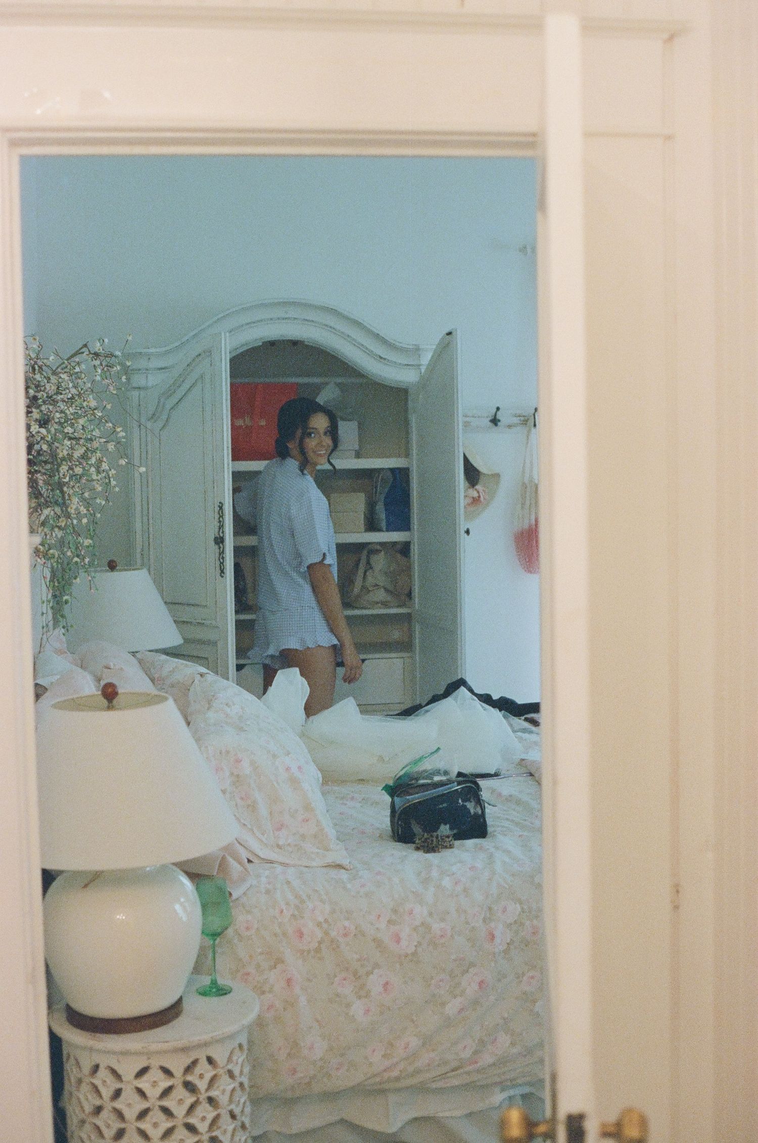 A vintage-style bedroom with white furniture, floral bedding, and an elegant armoire in soft natural lighting.