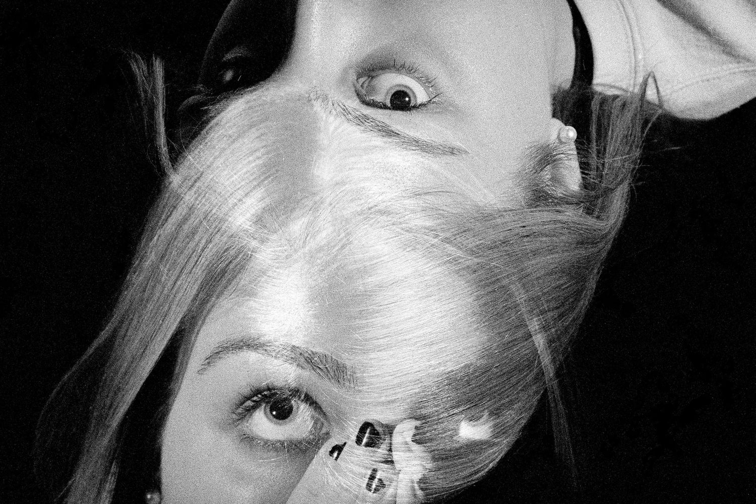 A black and white artistic portrait showing partial view of someone's face, hair and eye with dramatic lighting.