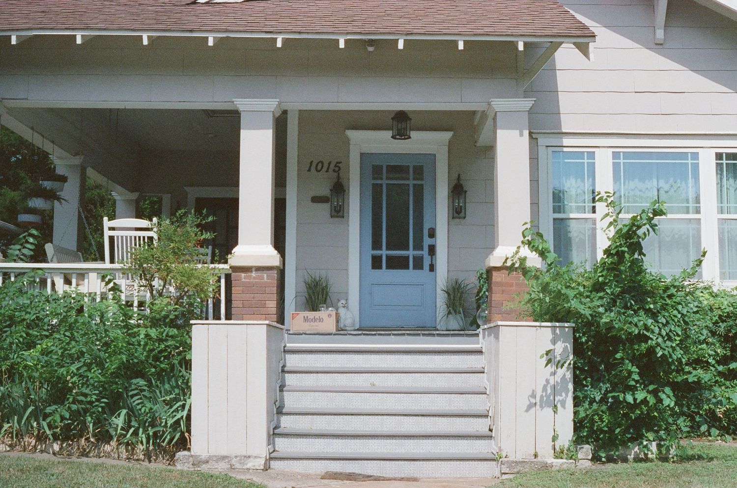 Charming craftsman style house exterior with white columns, blue door and concrete steps leading to covered front porch.
