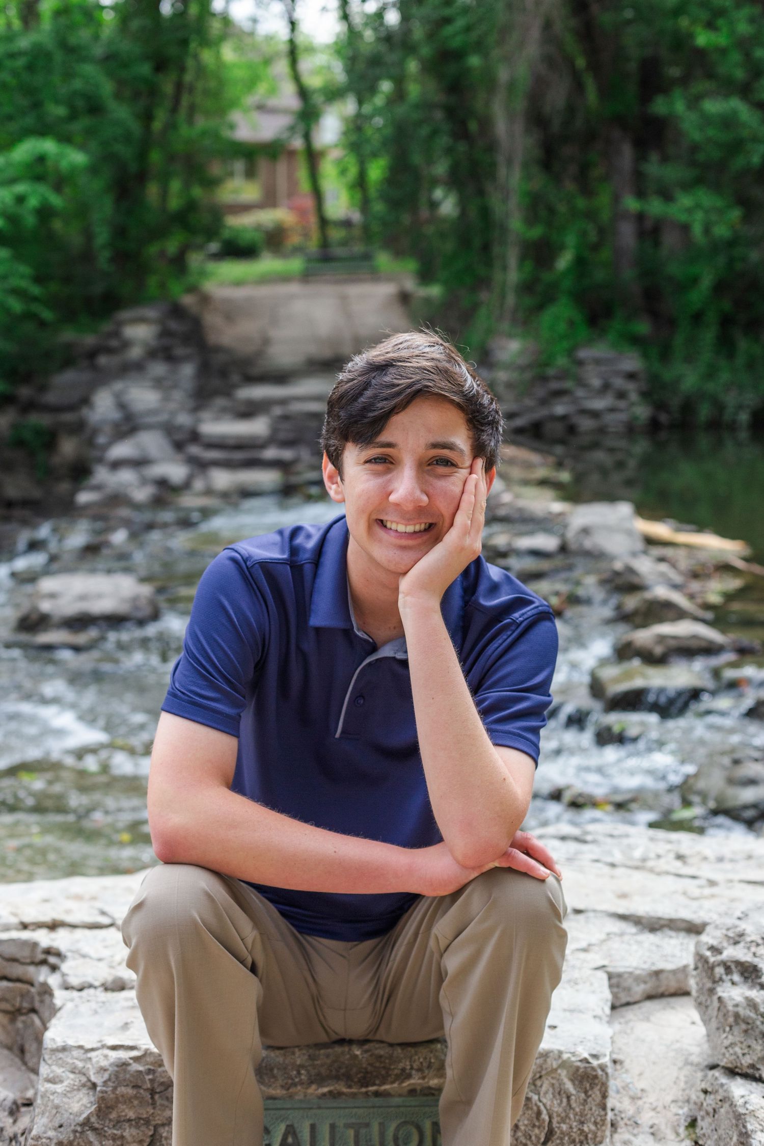 Someone in a navy blue polo shirt sits casually on stone steps surrounded by lush greenery and foliage.