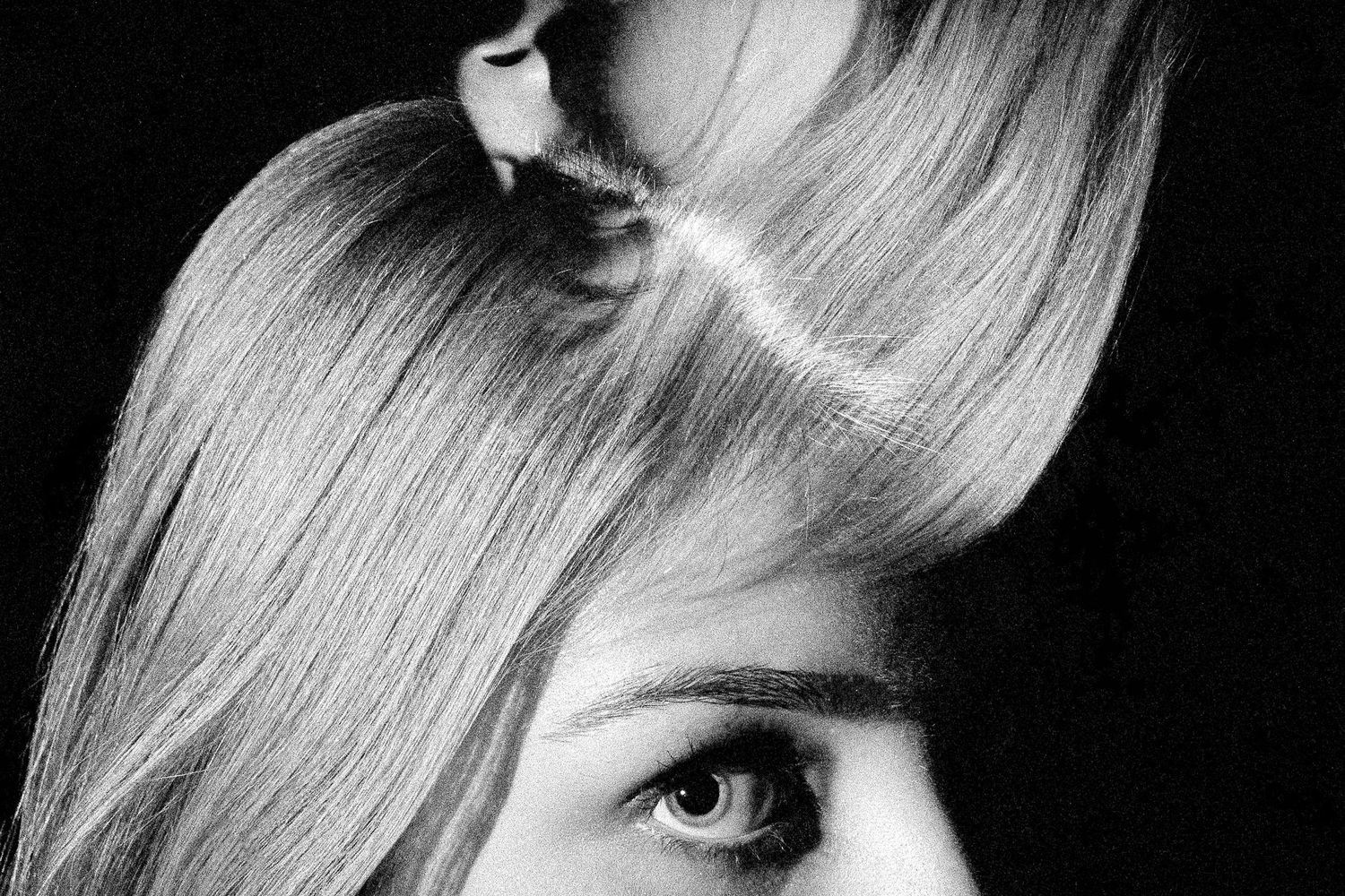 Black and white close-up artistic portrait showing an eye and blonde hair against dark background.