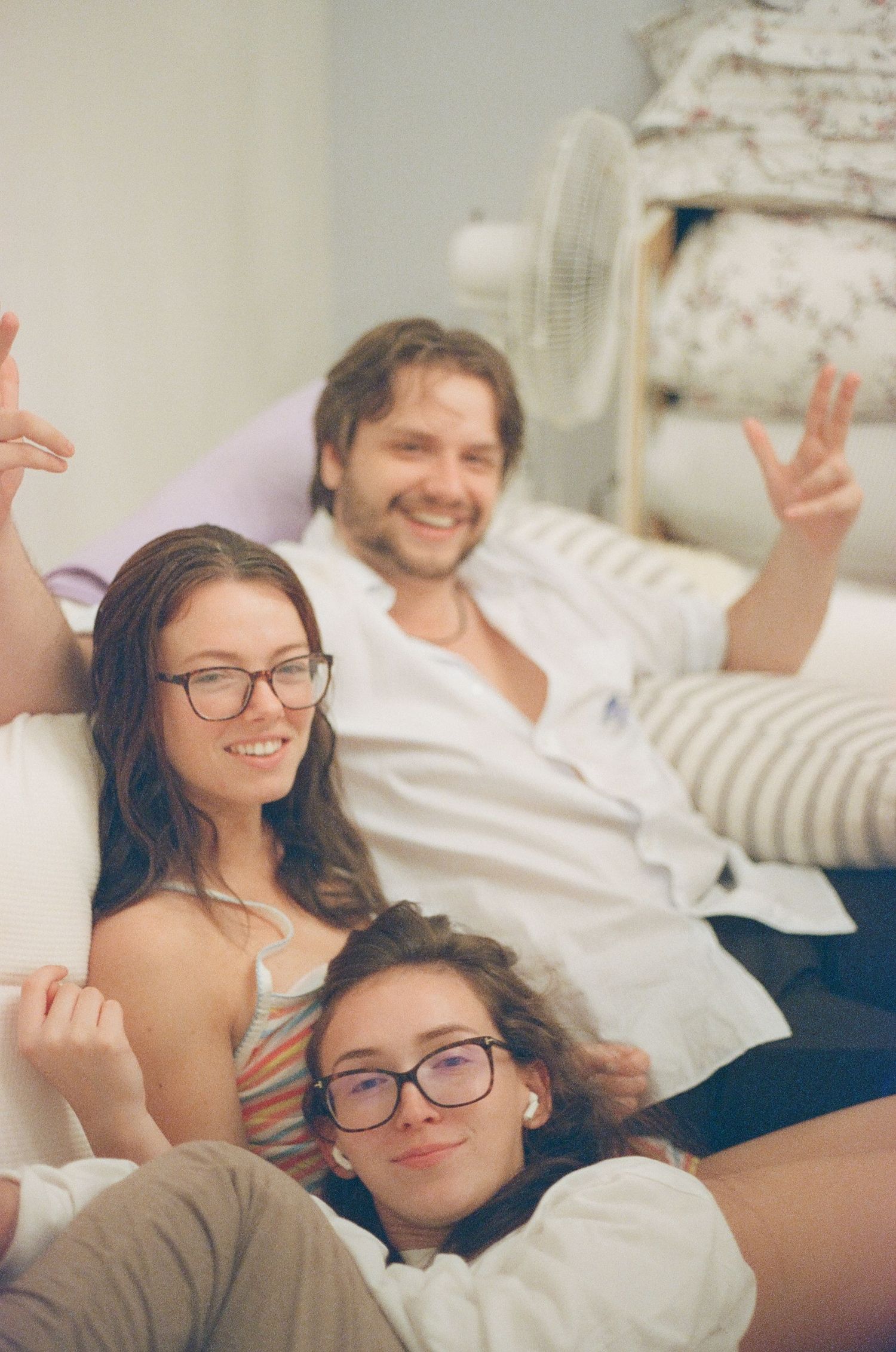 A candid photo of three people relaxing and smiling together on a bed in a cozy room.