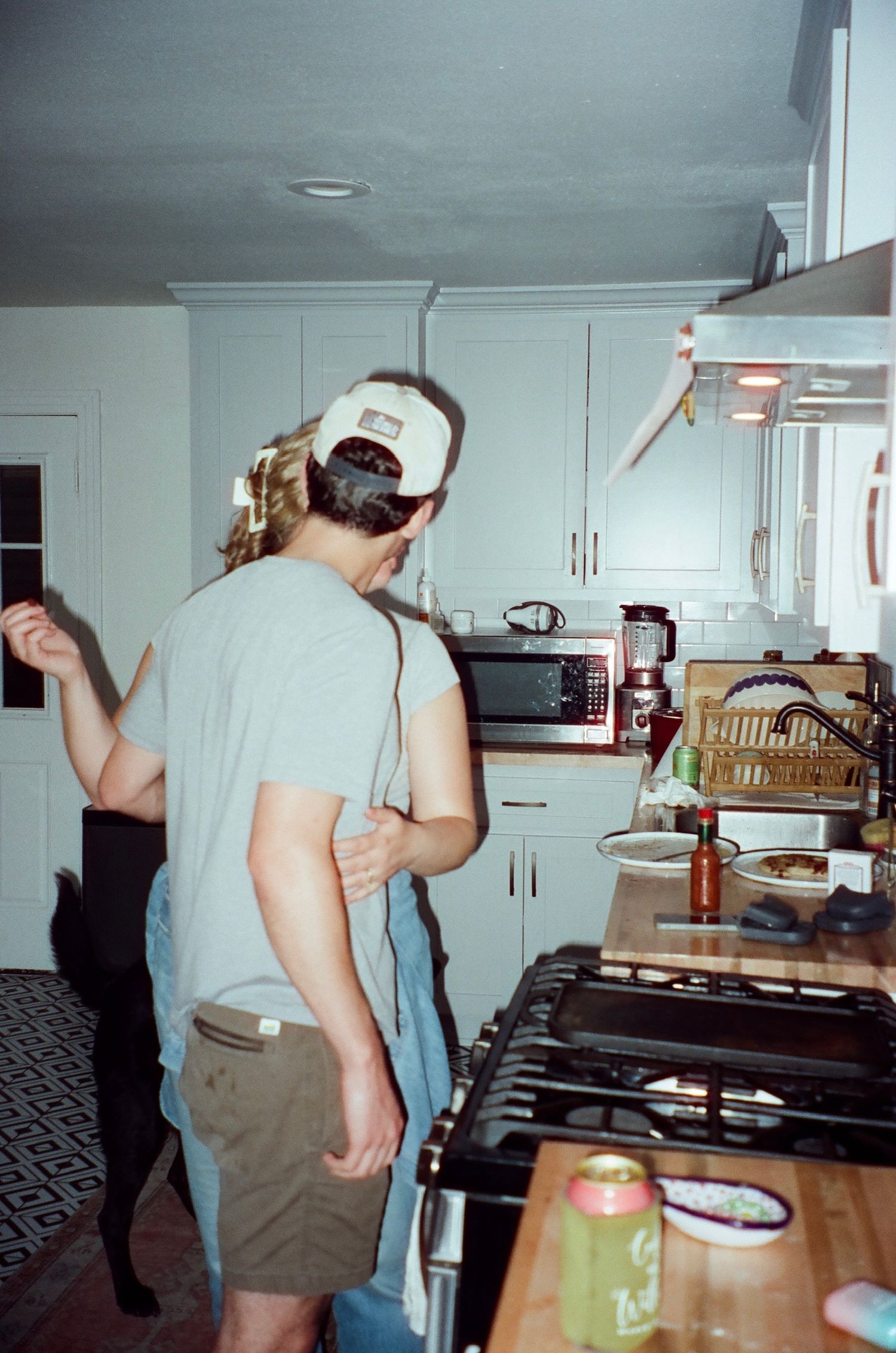 Group of friends dancing and celebrating in a dimly lit kitchen space with white cabinets and countertops visible.