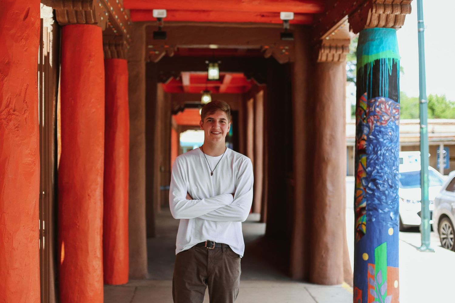 Person stands with crossed arms in red architectural corridor with turquoise accents and pillars.