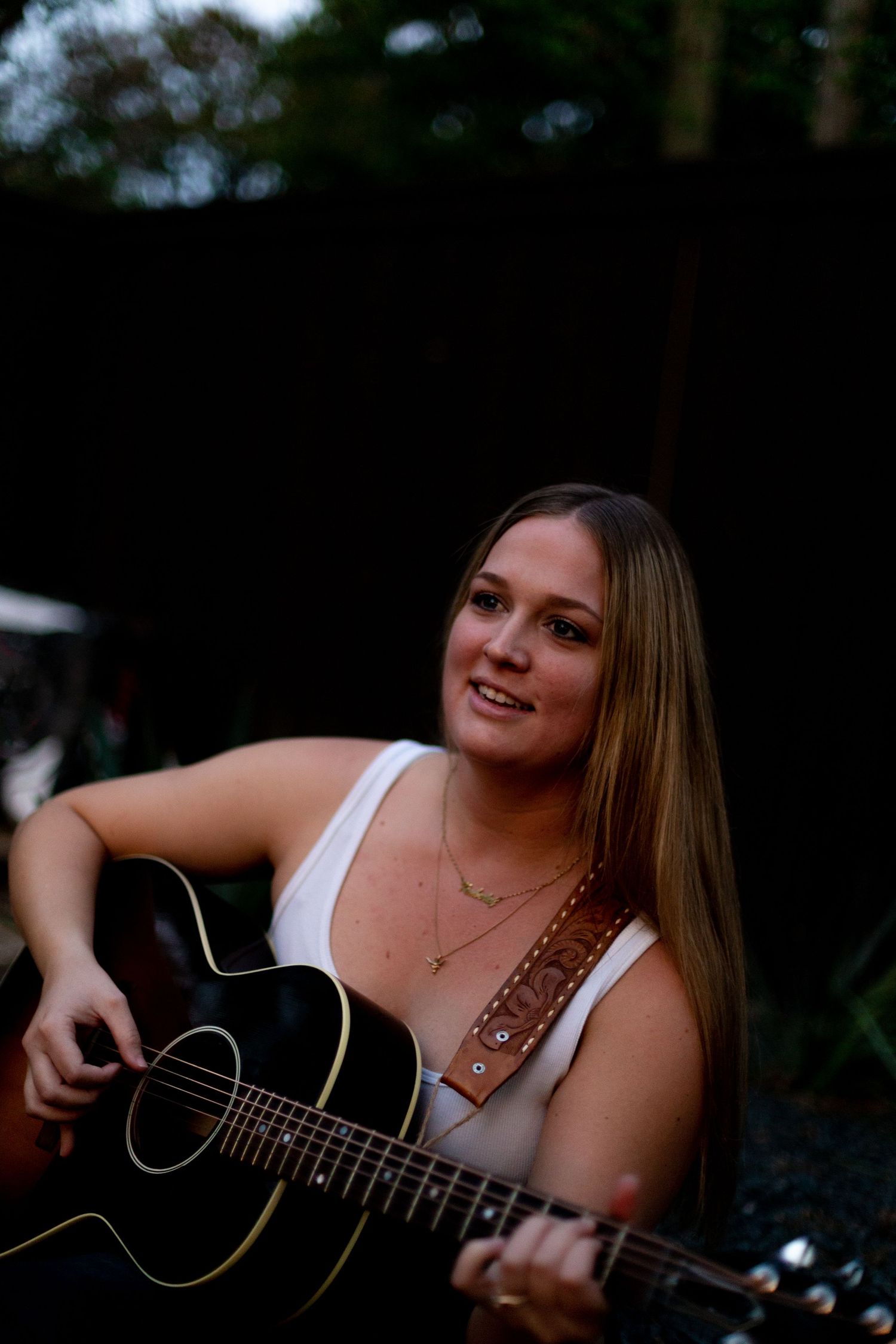 A musician performing on acoustic guitar outdoors with natural lighting.
