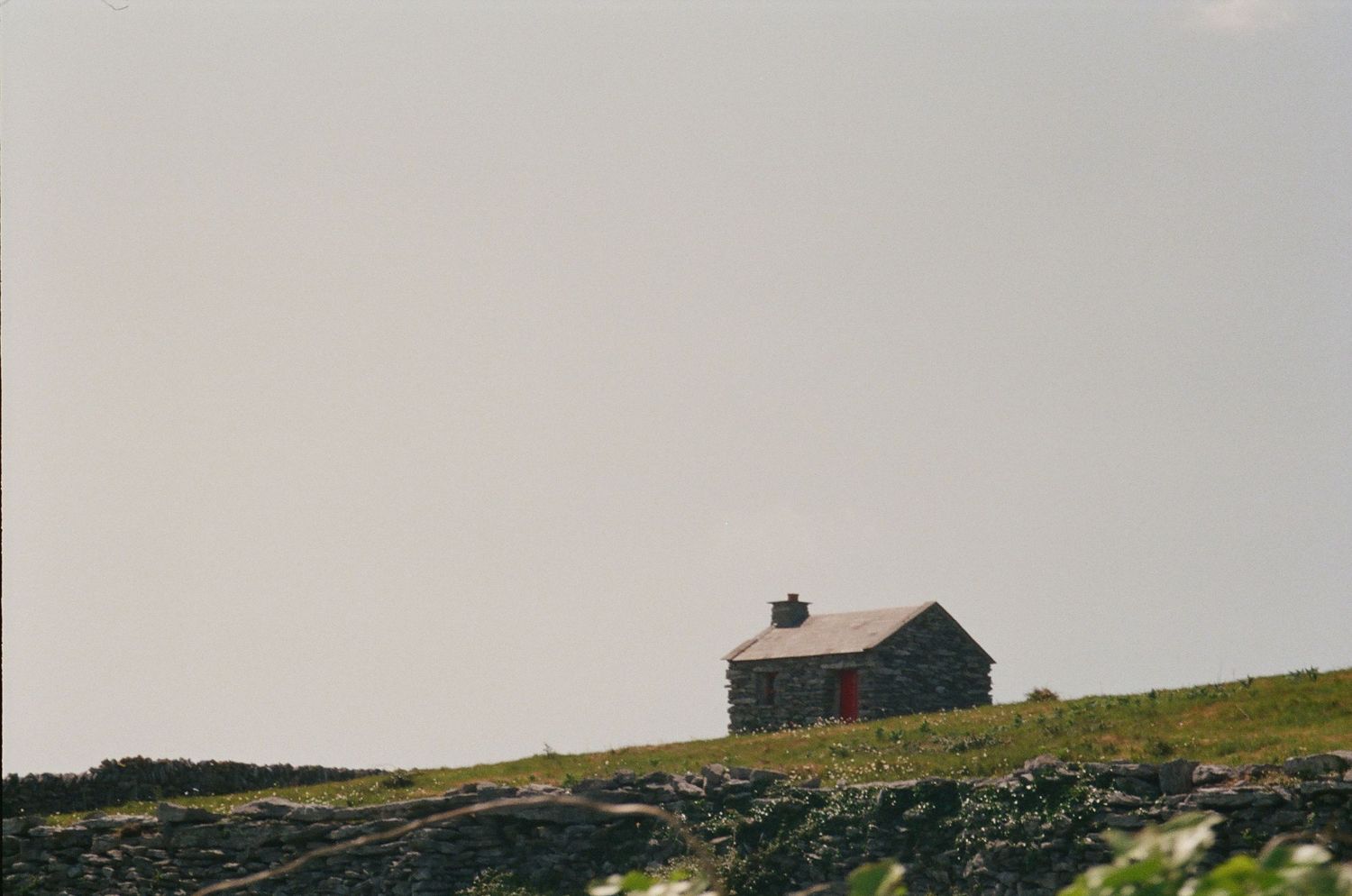 A solitary rustic barn stands silhouetted against the sky on a grassy hilltop overlooking rugged terrain.