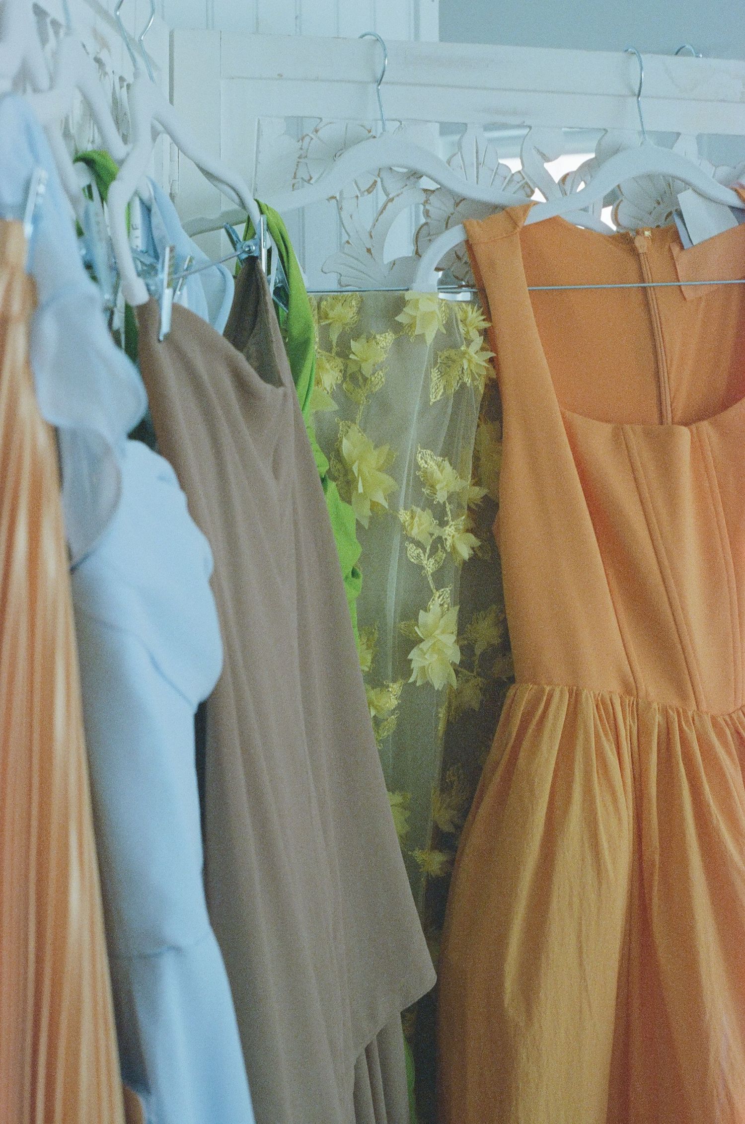 Pastel colored dresses and clothing hanging on display with soft peach, blue and beige tones against a light background.