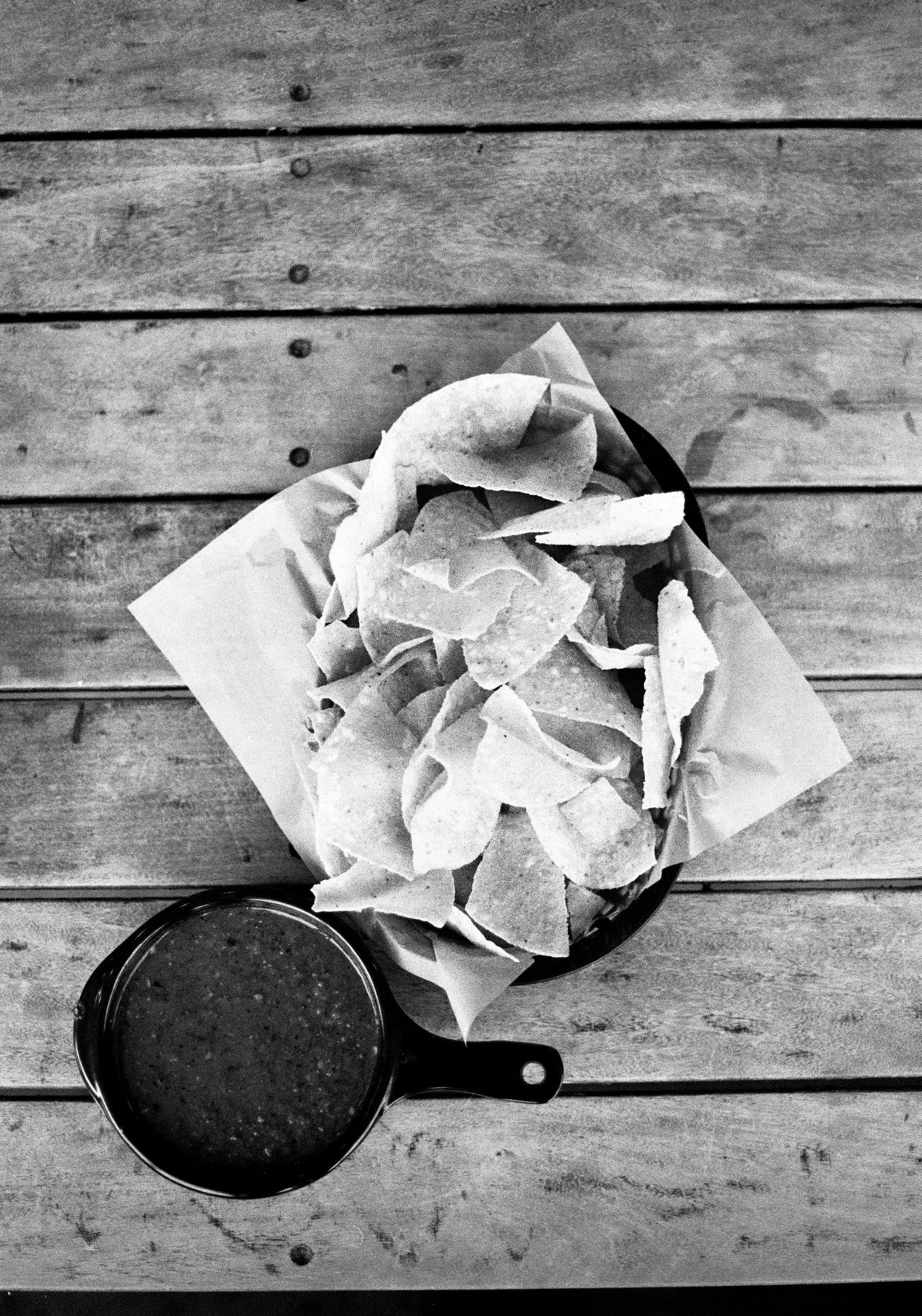 Black and white photograph of crumpled paper beside a cast iron skillet on rustic wooden planks.