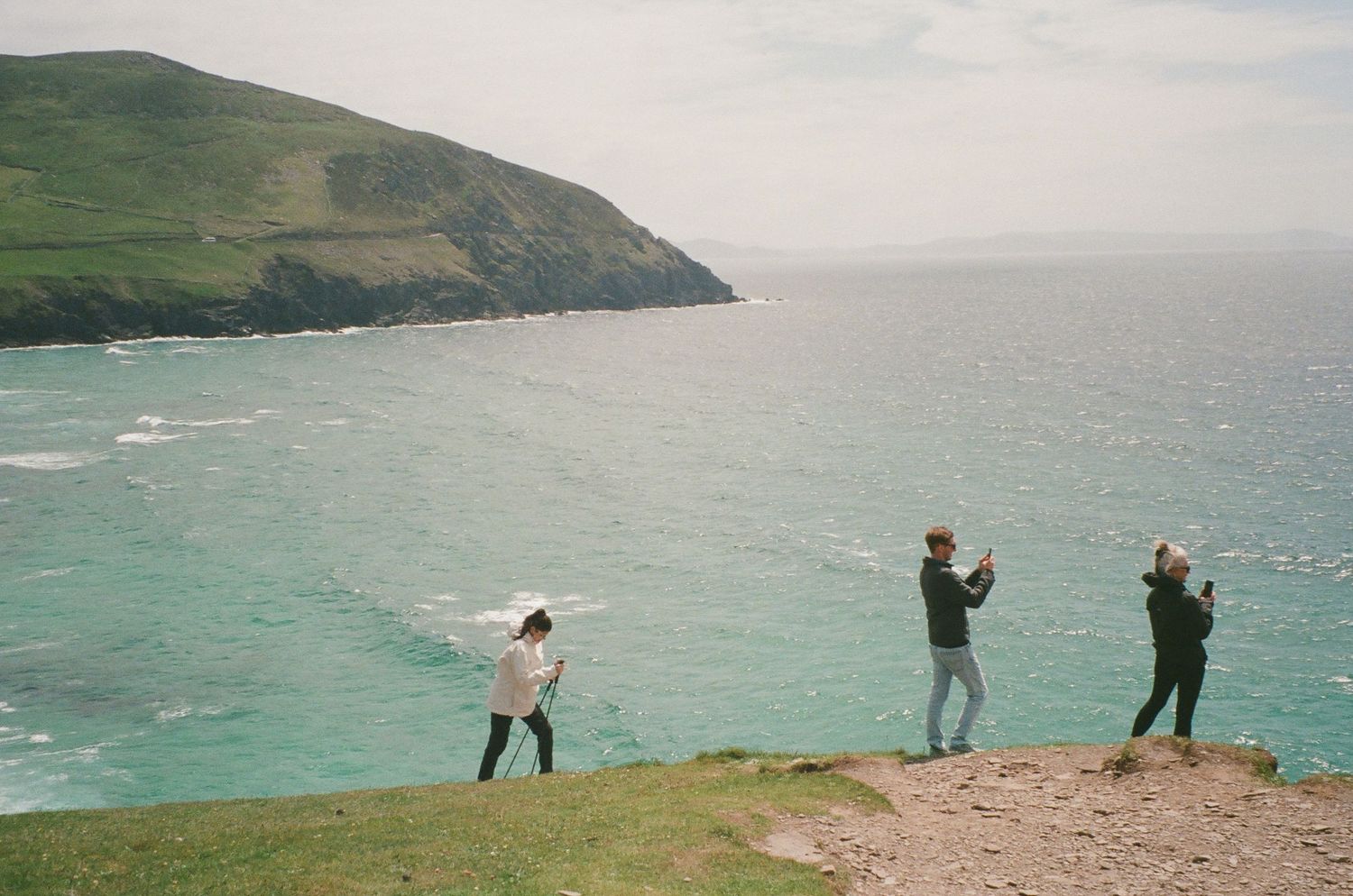 A series of coastal landscape photos shows people walking along dramatic cliffside paths overlooking turquoise waters.