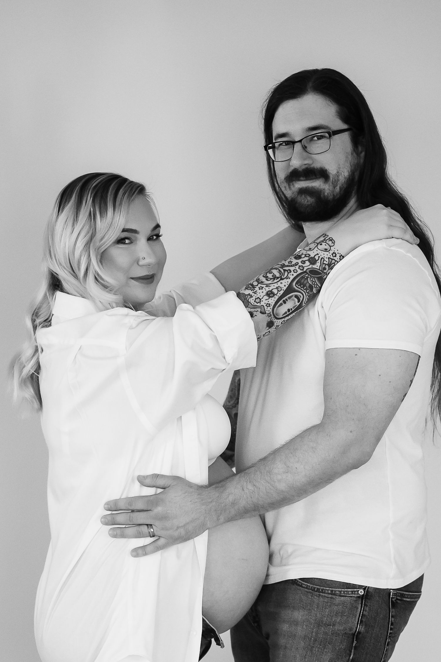 Black and white portrait of a couple in white shirts posing together in a studio setting.