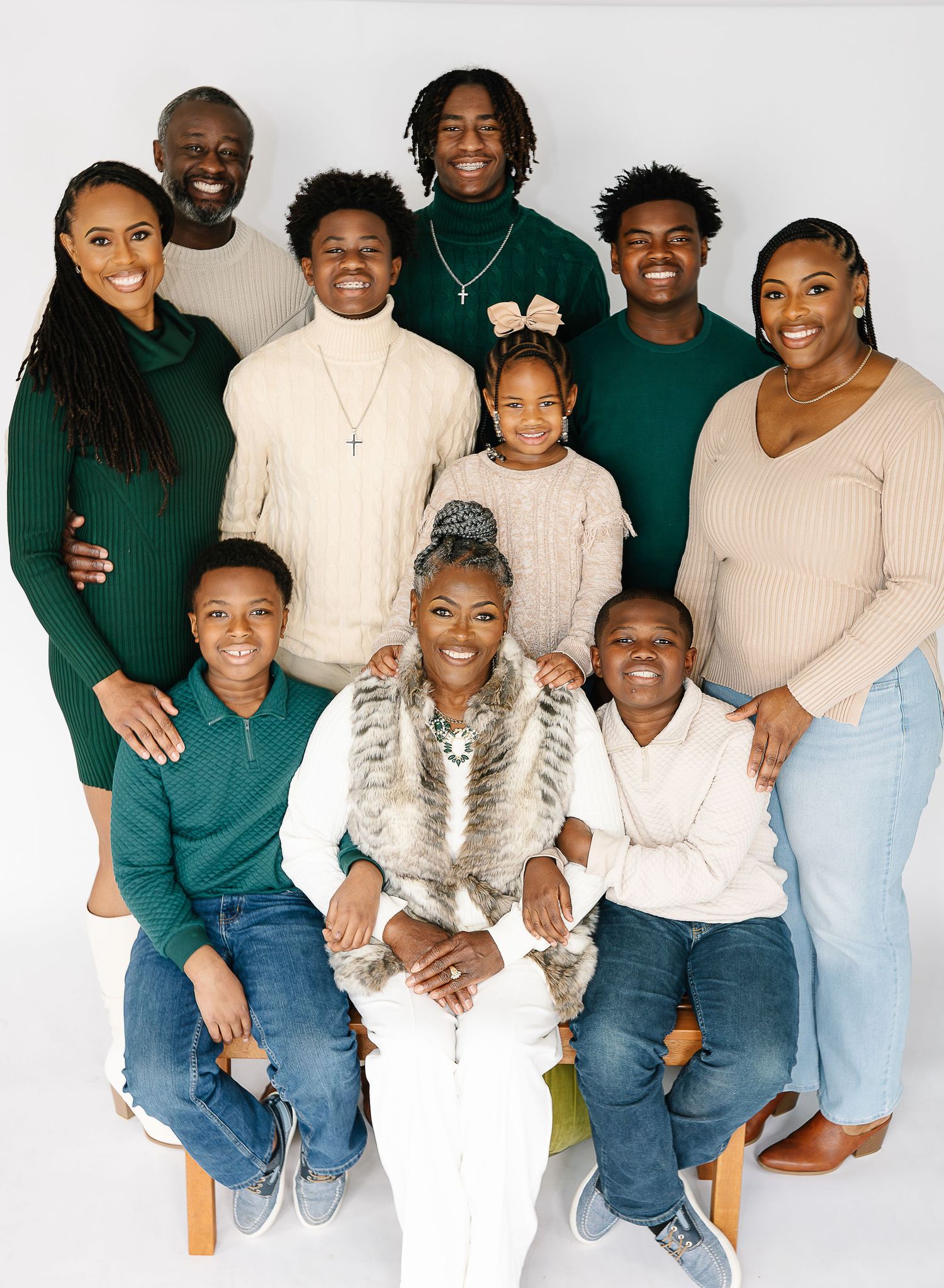 Studio family portrait with everyone wearing coordinated green, cream and denim outfits.