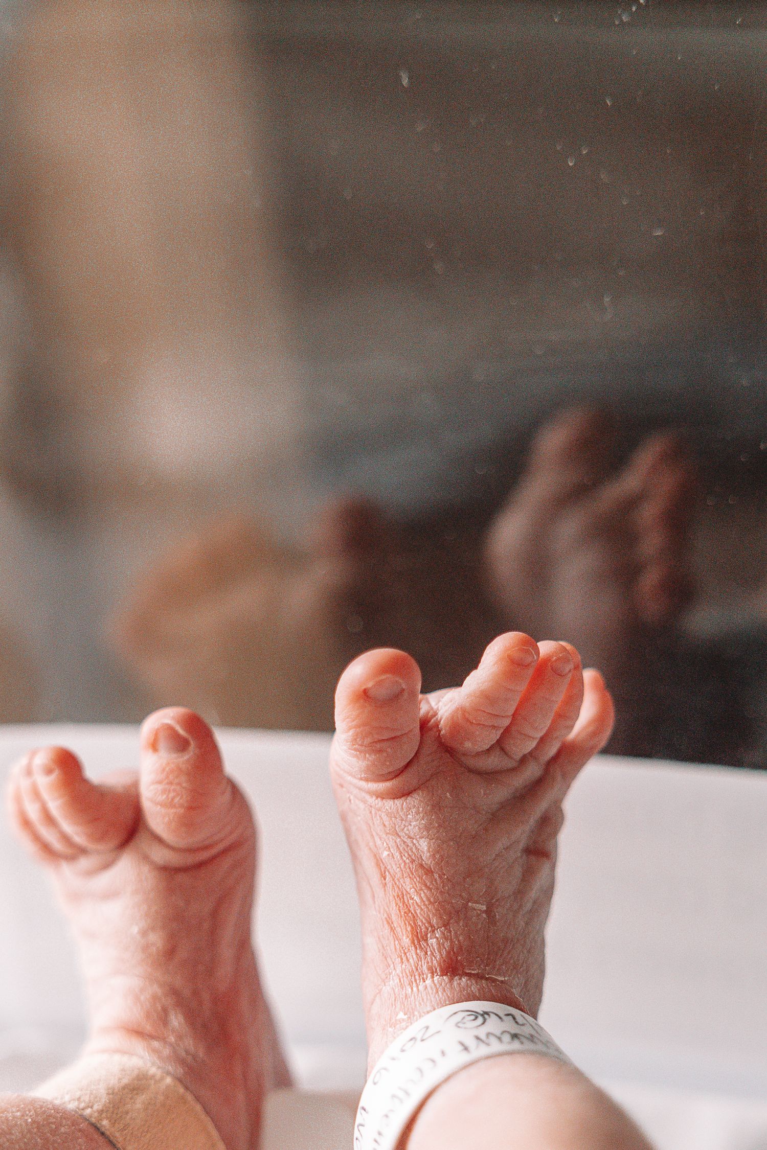 Close-up of tiny newborn baby feet with wrinkled skin wearing white socks against a light background.