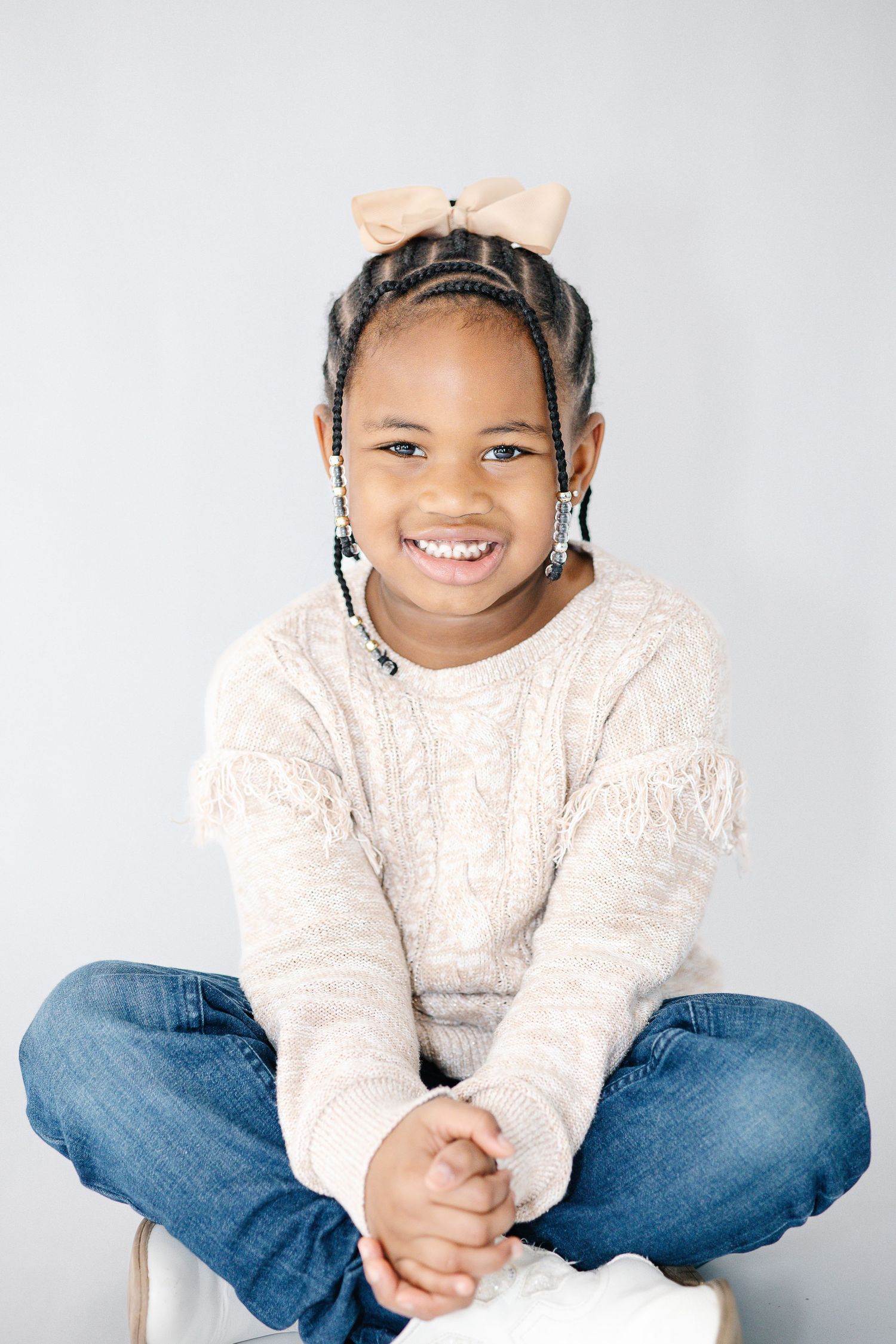 Person in a cream cable knit sweater and jeans sits casually against a light background.