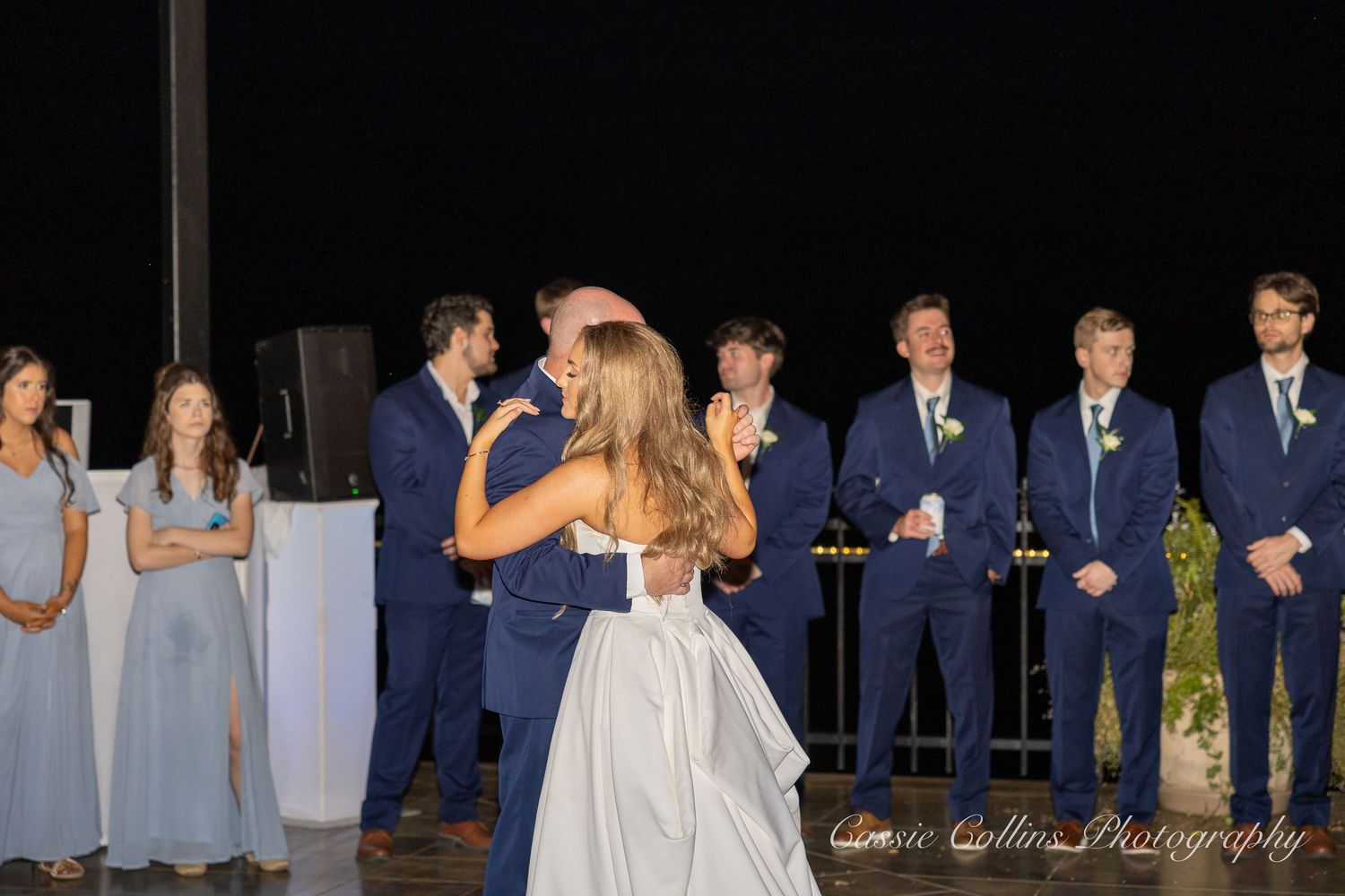 Wedding party stands in a row wearing navy suits and gray dresses during an outdoor ceremony.