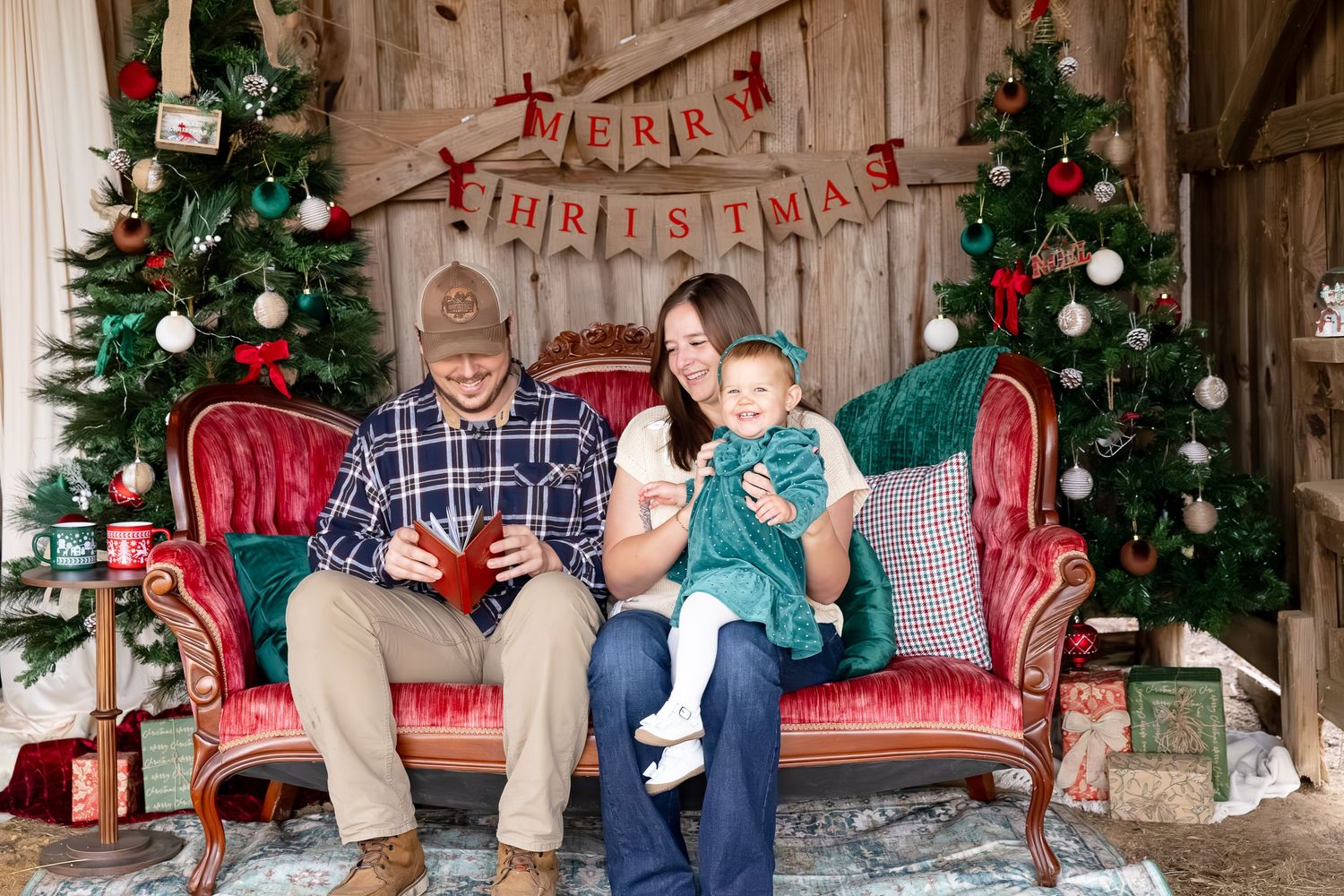 A rustic Christmas photo session with decorated trees and red decor in a wooden barn setting.
